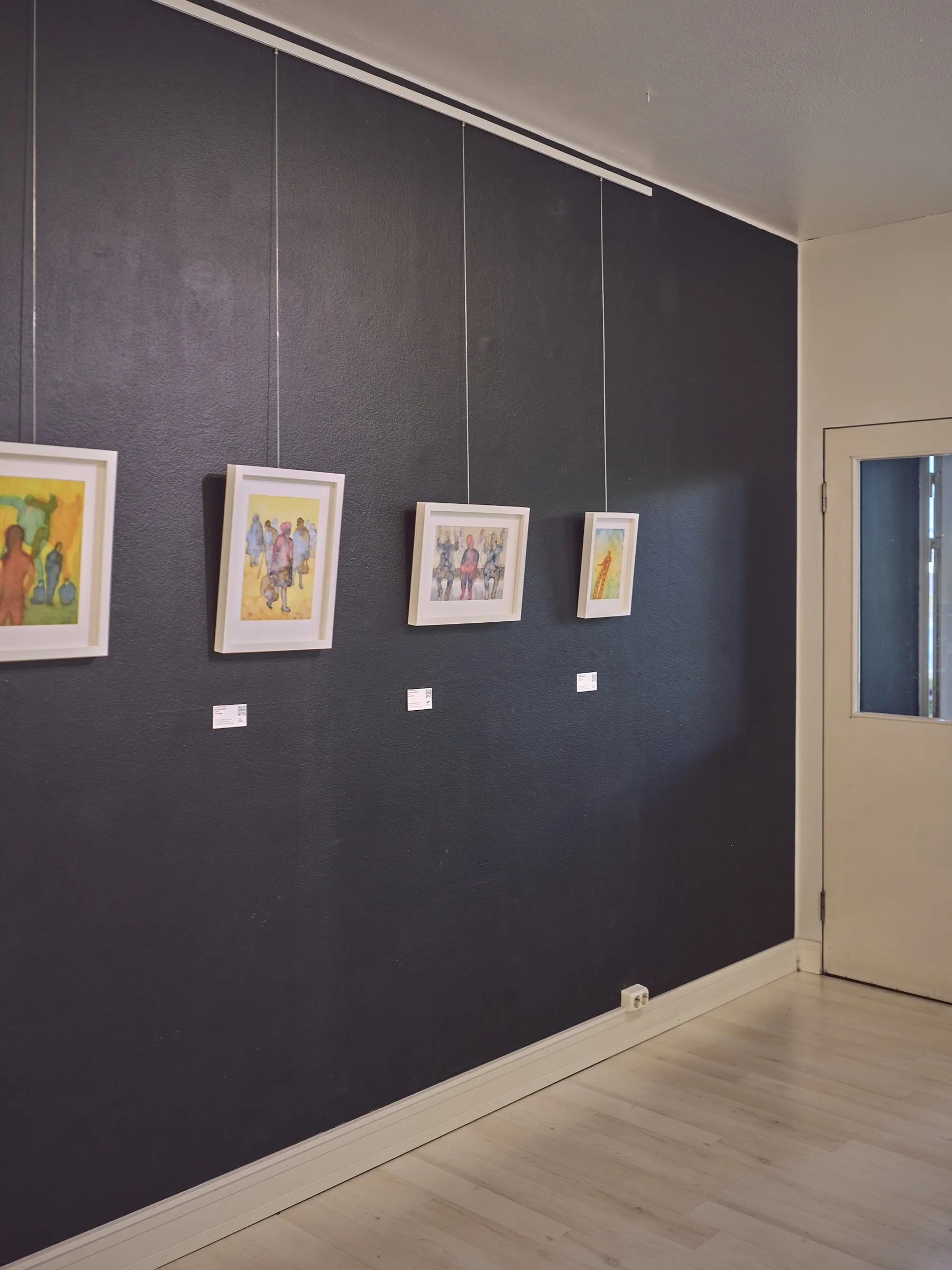 Dark gallery wall with four small watercolours in light frames, portrait format