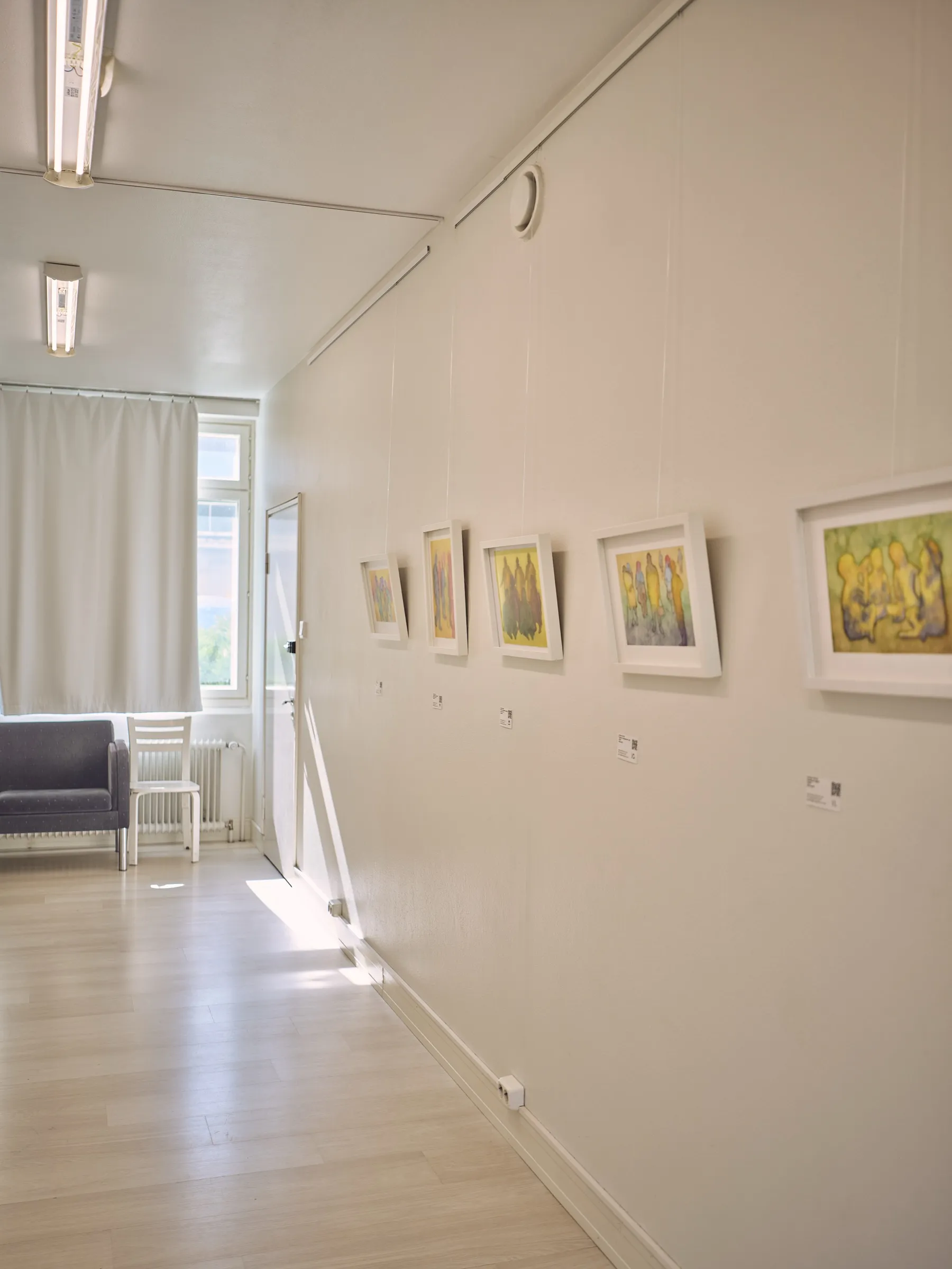 Long light wall with a row of small framed watercolours, a blue sofa at the back, portrait format