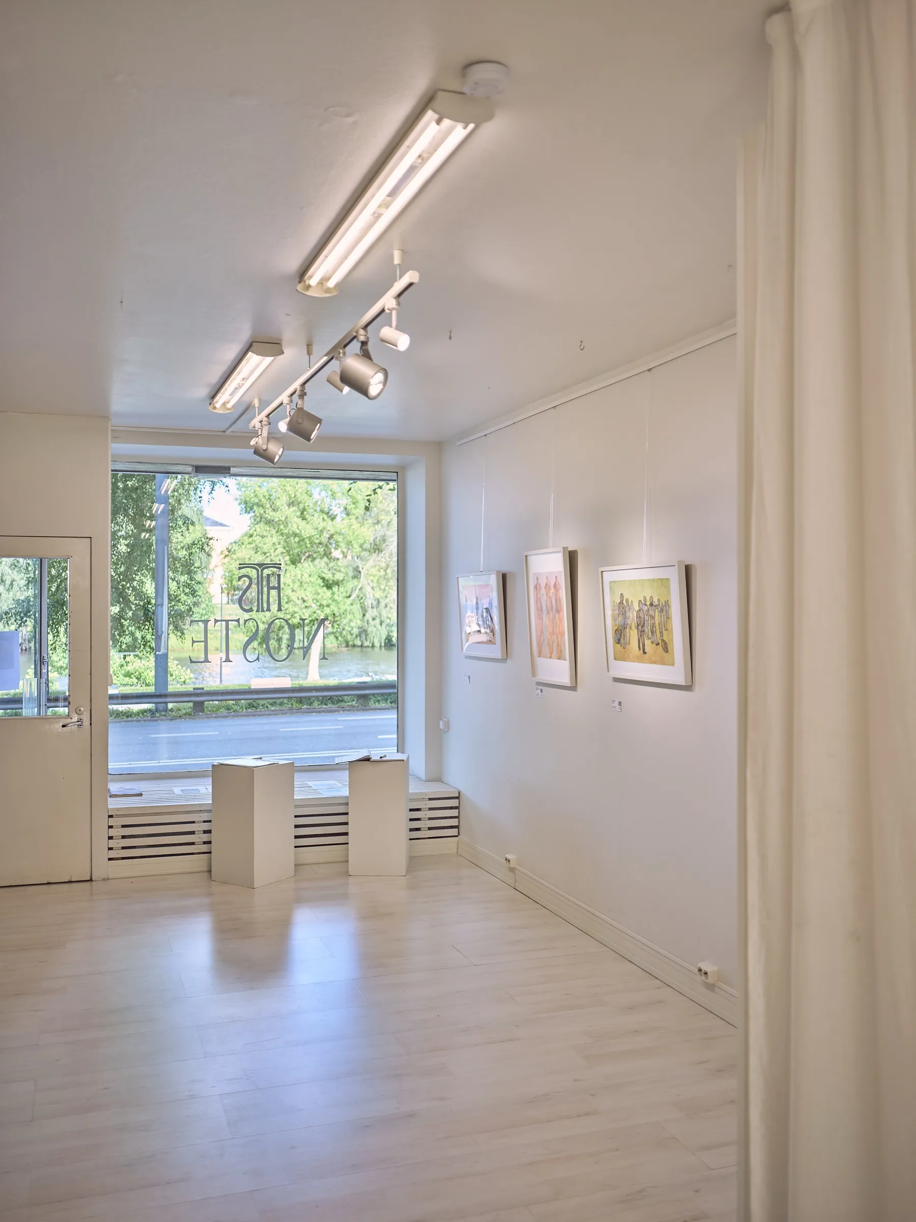 Gallery room with ceiling spots, plinths by the window, curtain on the right, portrait format
