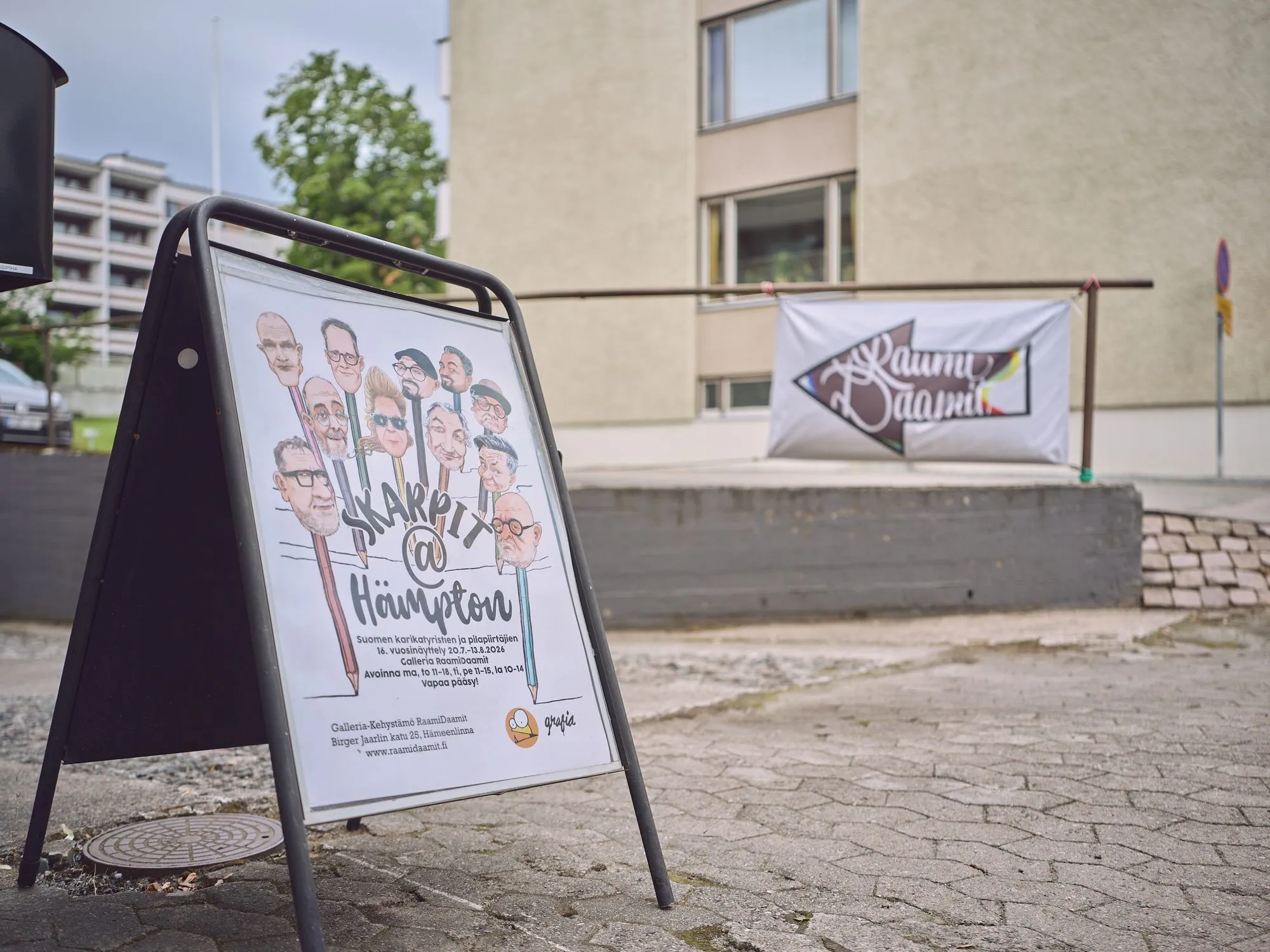 A sign at the door with the poster Skarpit @ Hämpton, showing many caricature faces