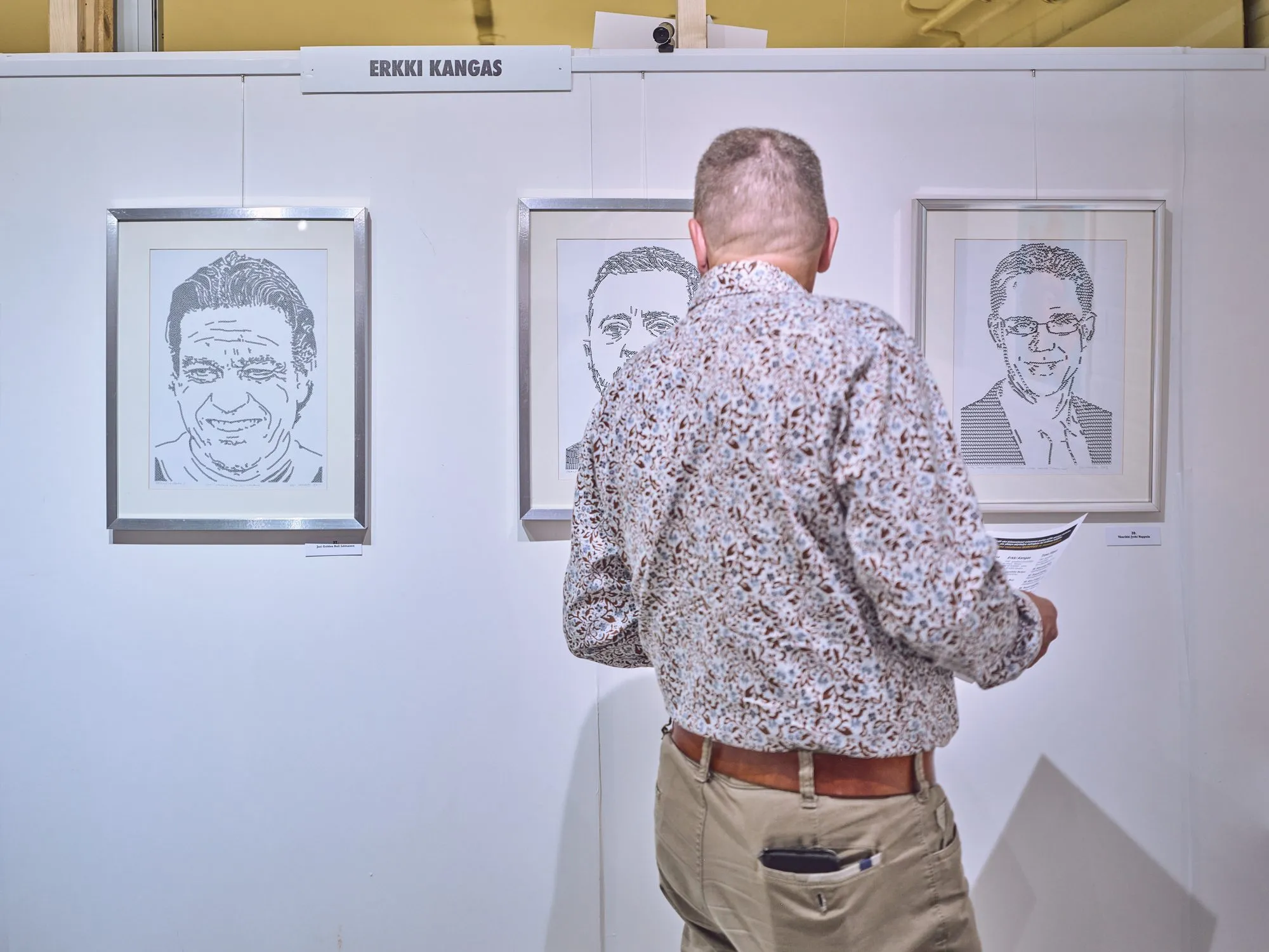 A visitor in front of Erkki Kangas's wall with several portraits in black and white