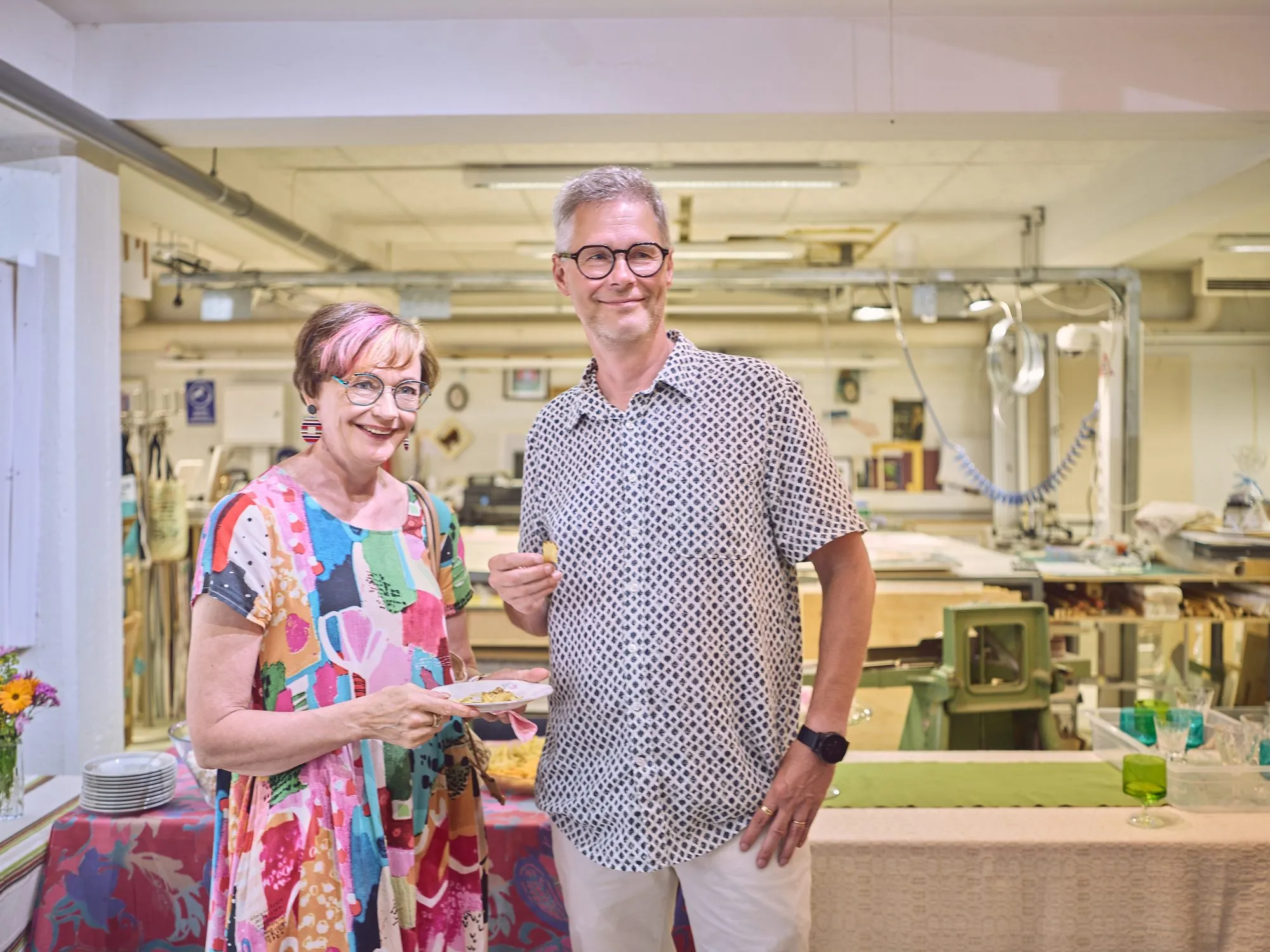 Two people talking in the framing workshop, tools and a laid table in the background