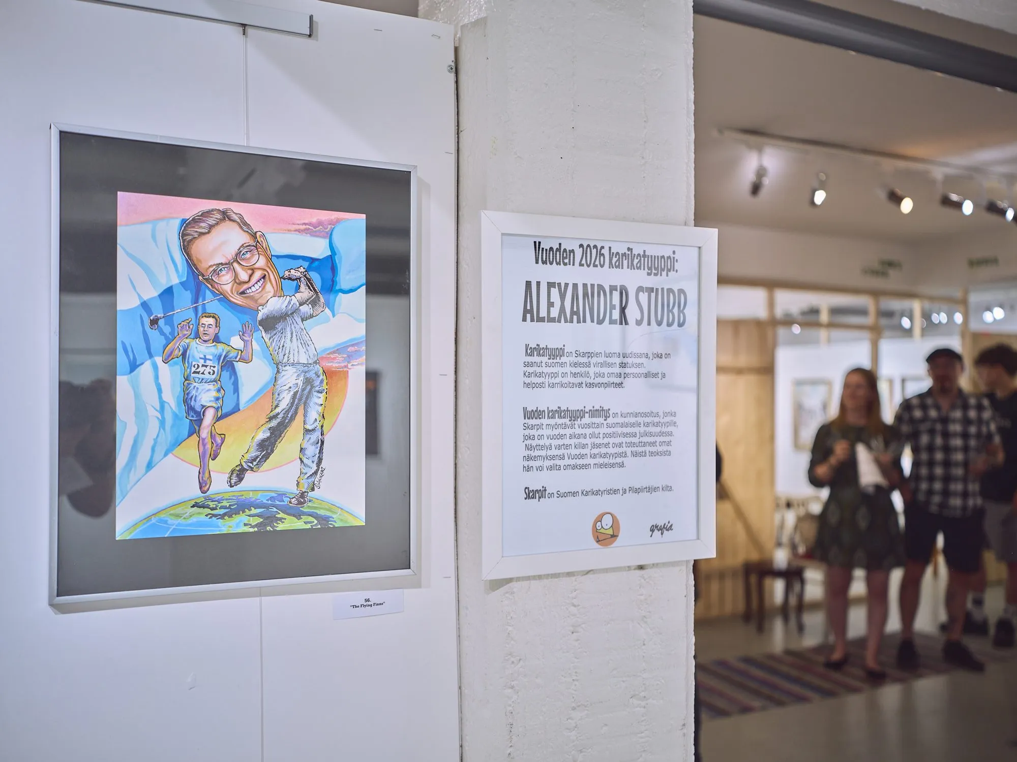 Sign reading Vuoden 2026 karikatyyppi Alexander Stubb, beside a caricature of Stubb as runner and golfer