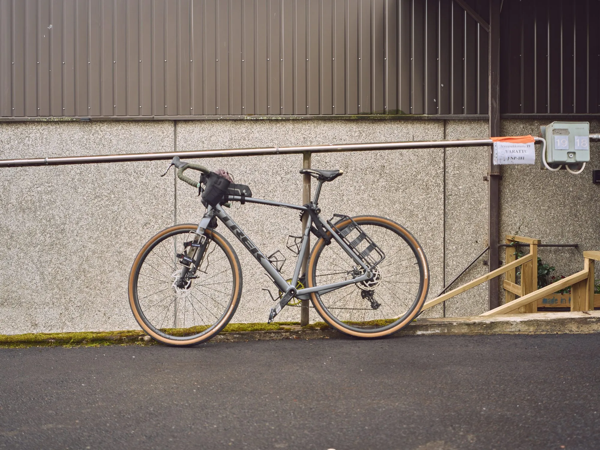 A bicycle leans against a concrete wall in front of the gallery, an empty summer street