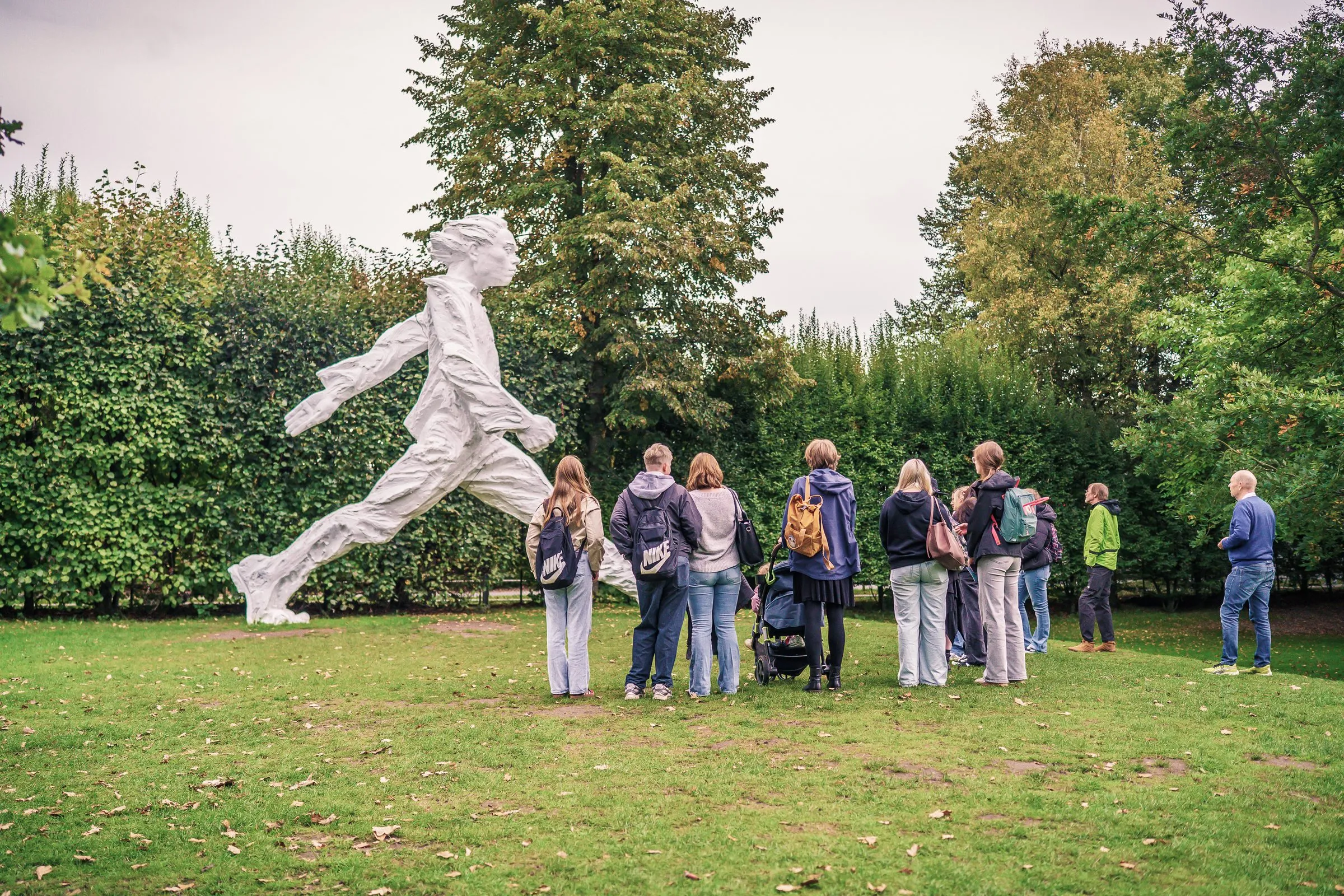 A white, larger-than-life running figure on the lawn, a group of visitors in front of it