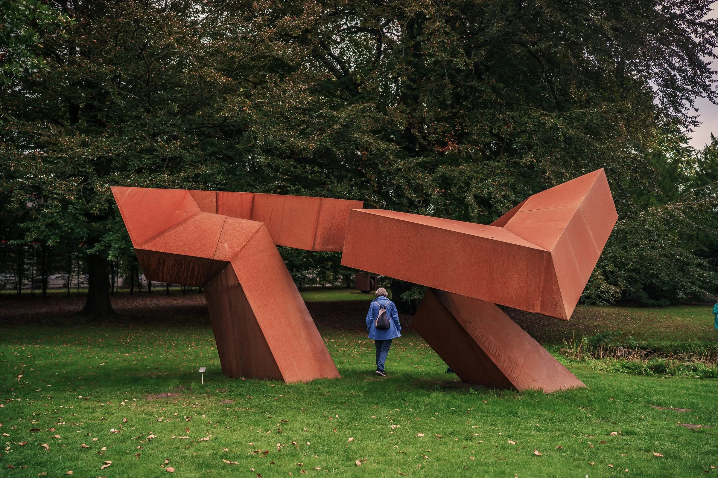 A large sculpture of red weathering steel with angular forms, a visitor beneath it