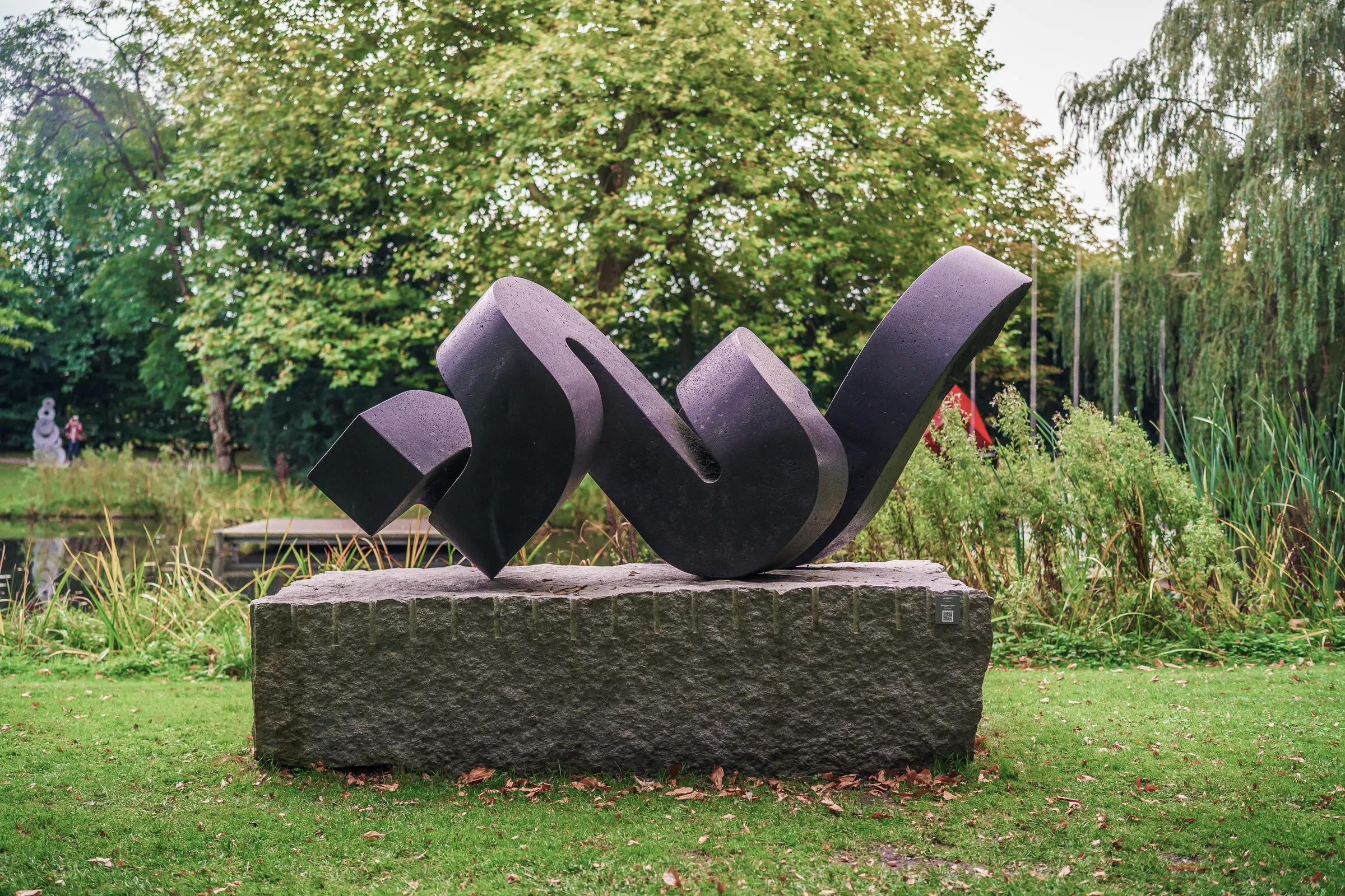 A black, winding sculpture like a folded ribbon on a grey stone plinth