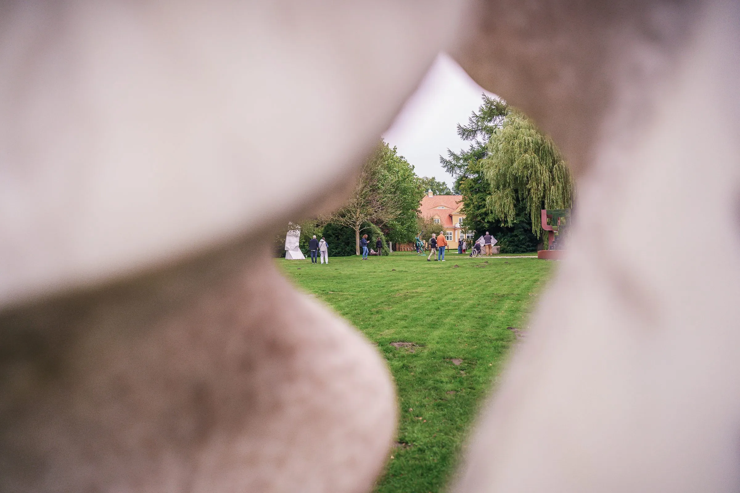 A view through an opening in a pale stone sculpture out onto lawn and trees