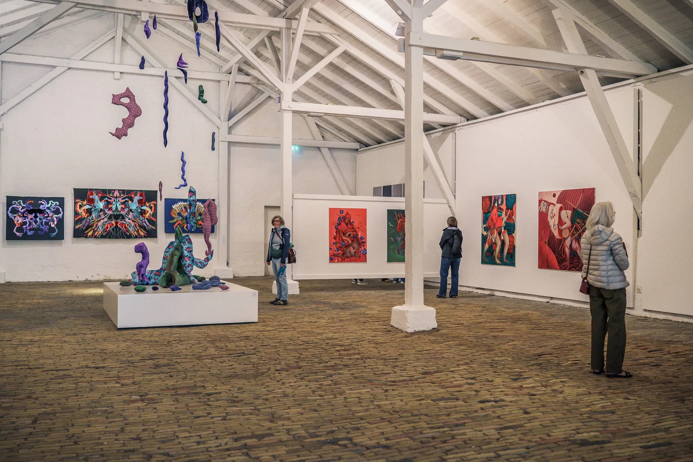 A bright hall with a white timber roof, colourful paintings on the walls, a sculpture in the middle