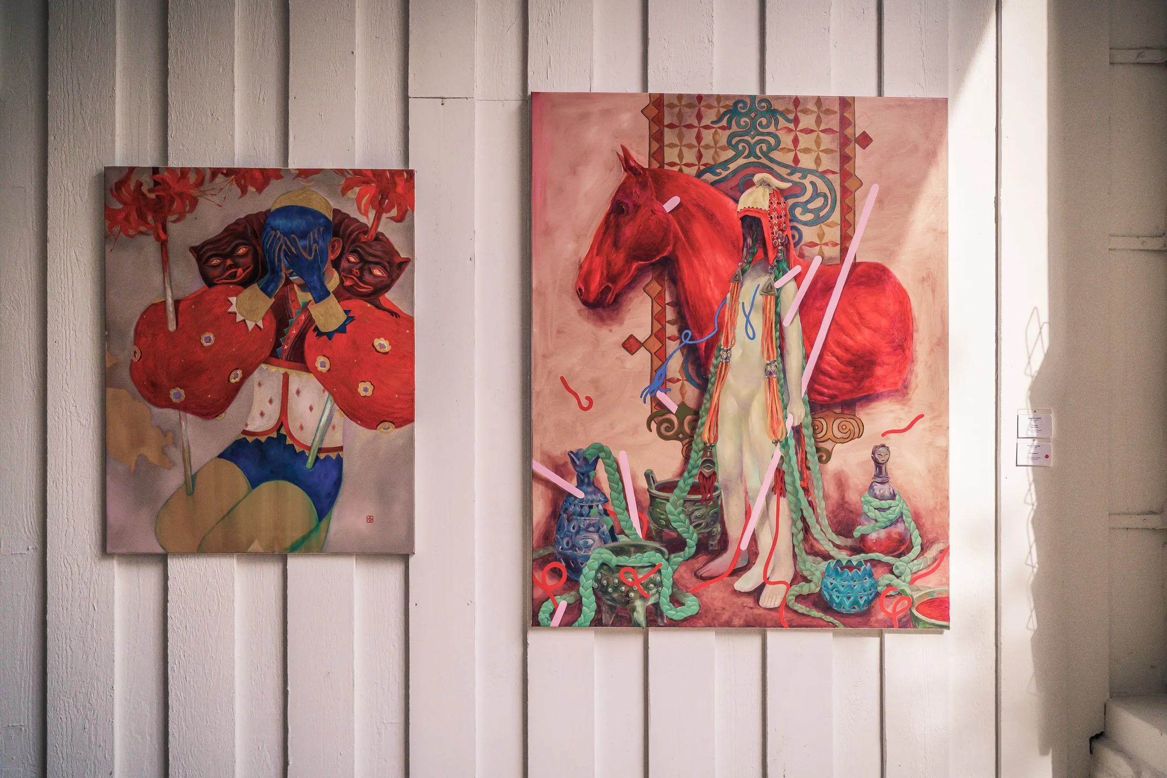 Two paintings side by side, one with a figure in red, one with a red horse and a robed figure