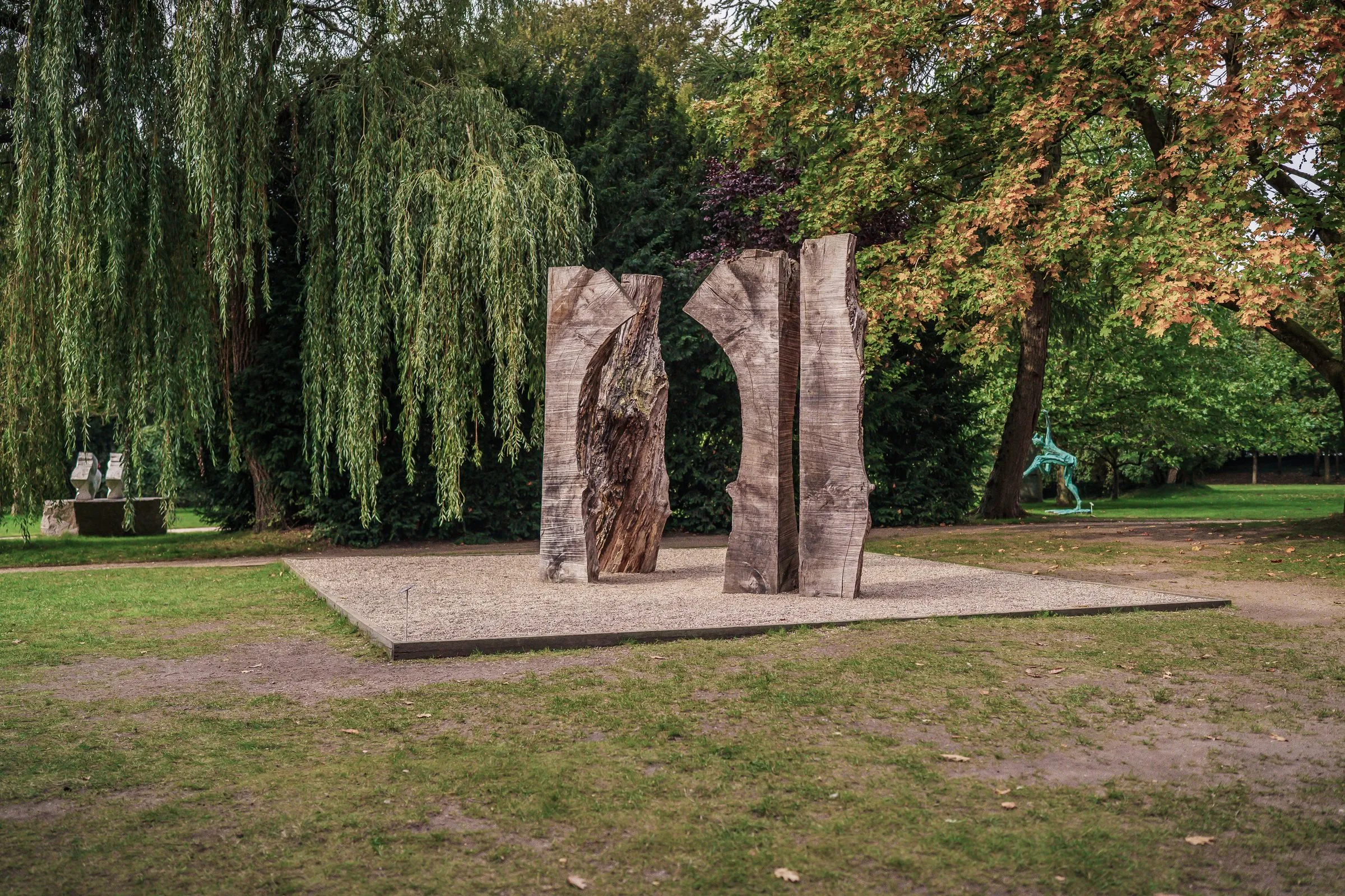 Two tall upright stone slabs on a pale field, weeping willows behind