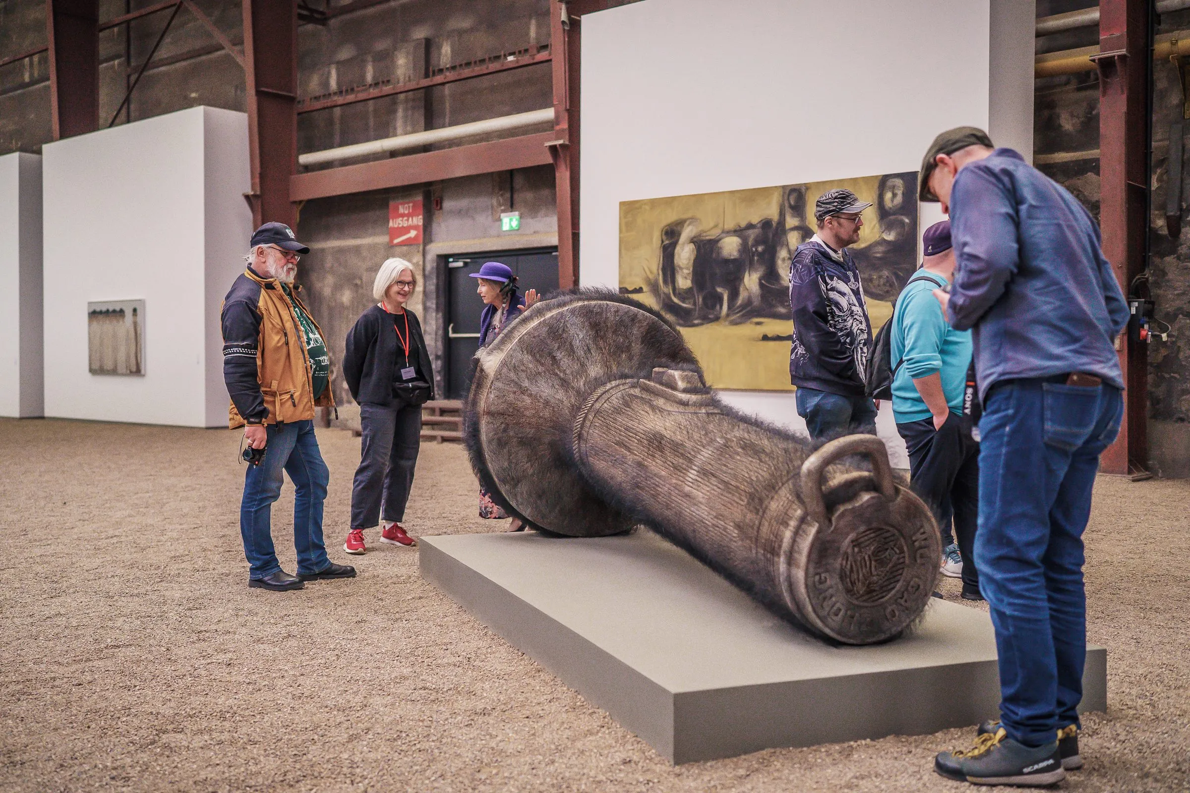 Visitors stand around a large reclining form of dark metal on a plinth