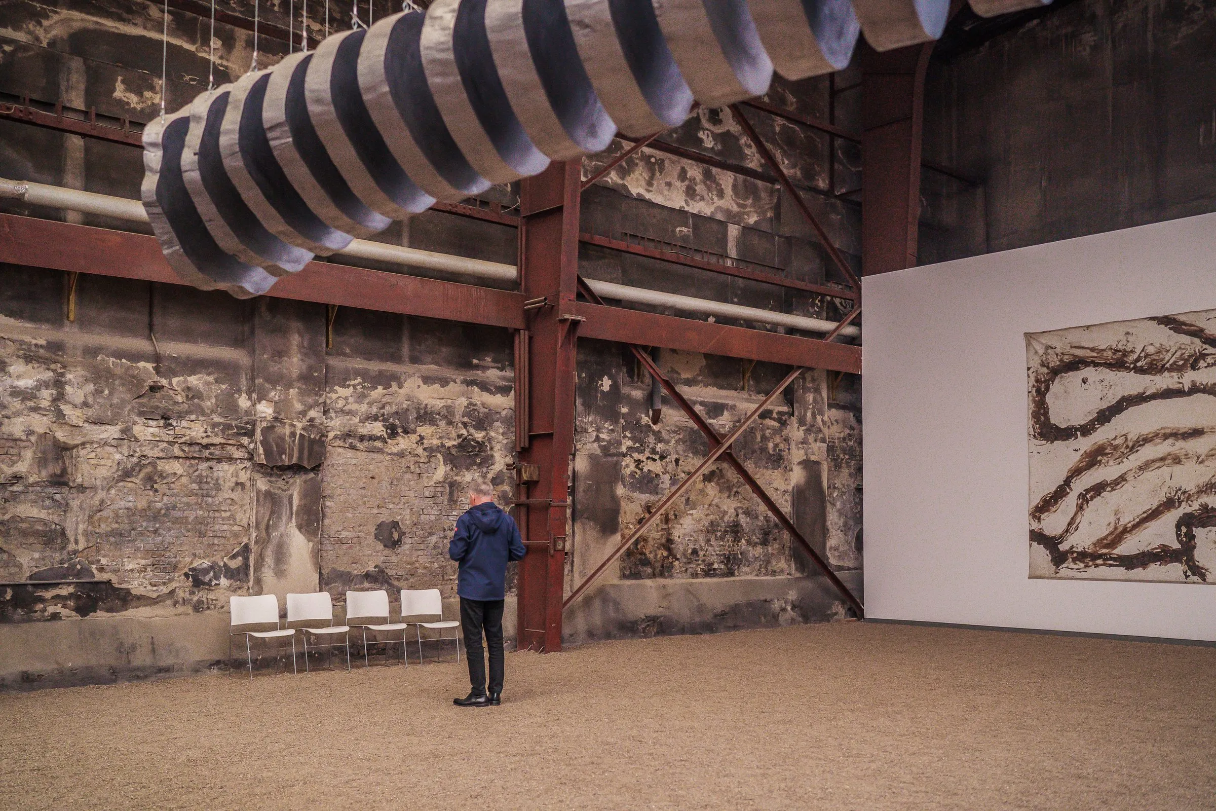 Old, rough hall walls with steel girders, a huge spiral above, a single visitor below