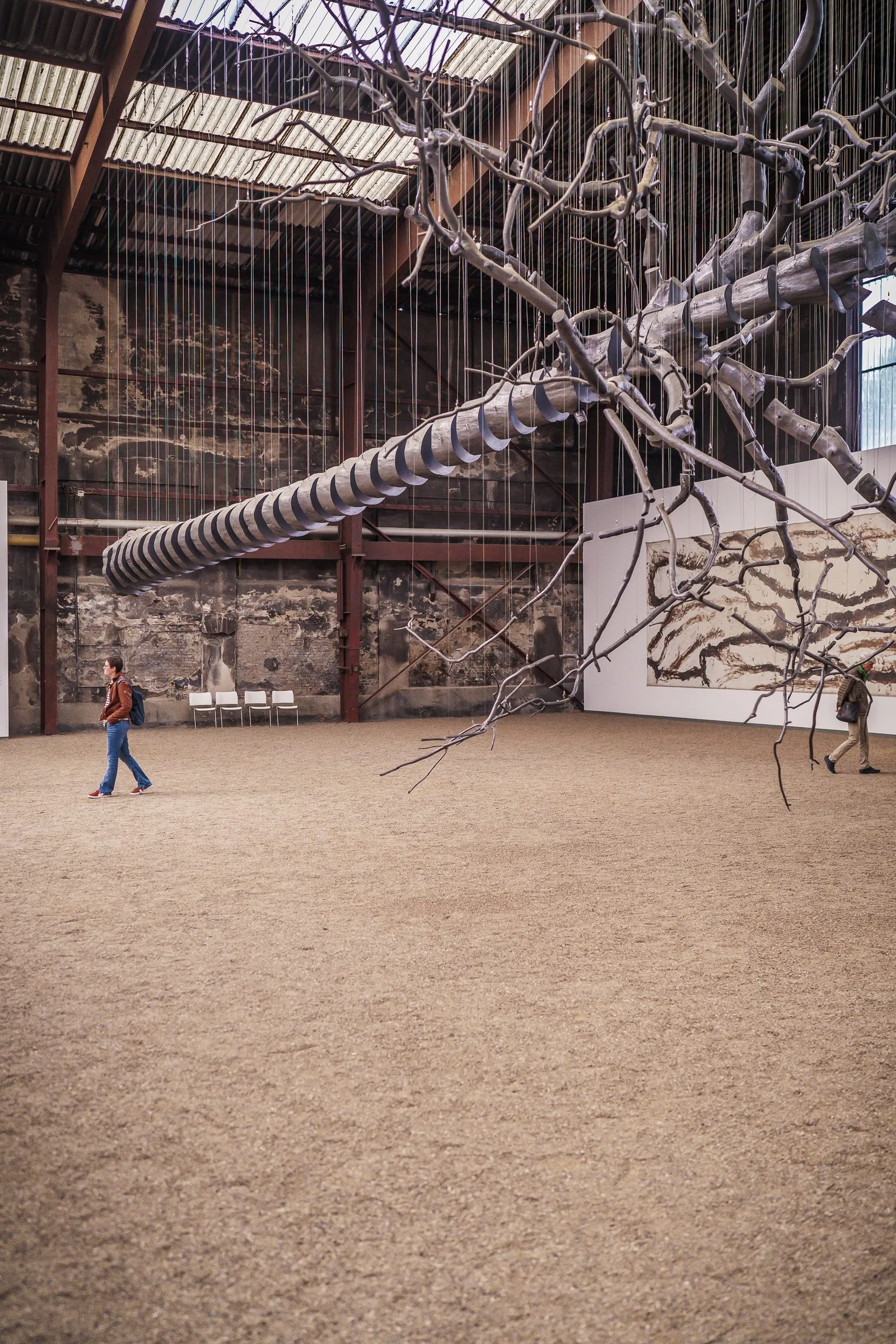 Portrait: bare branches and a long spiral float through the hall, a tiny person below