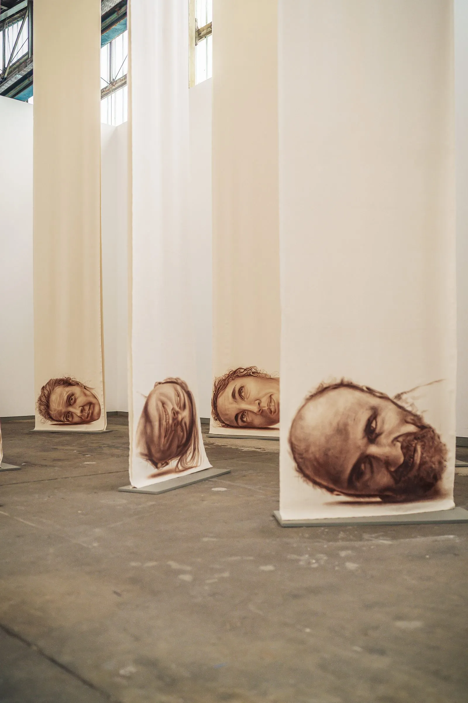 Portrait: long pale fabric banners hang from the ceiling, a painted face at the bottom of each
