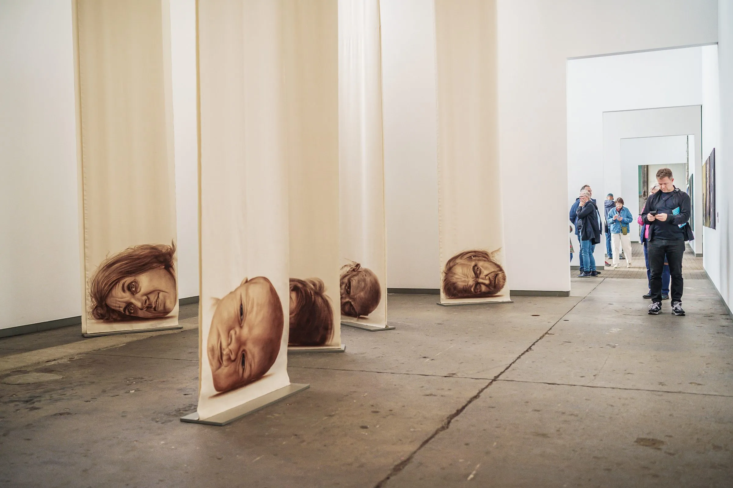Many fabric banners with faces in the room, visitors in a doorway behind