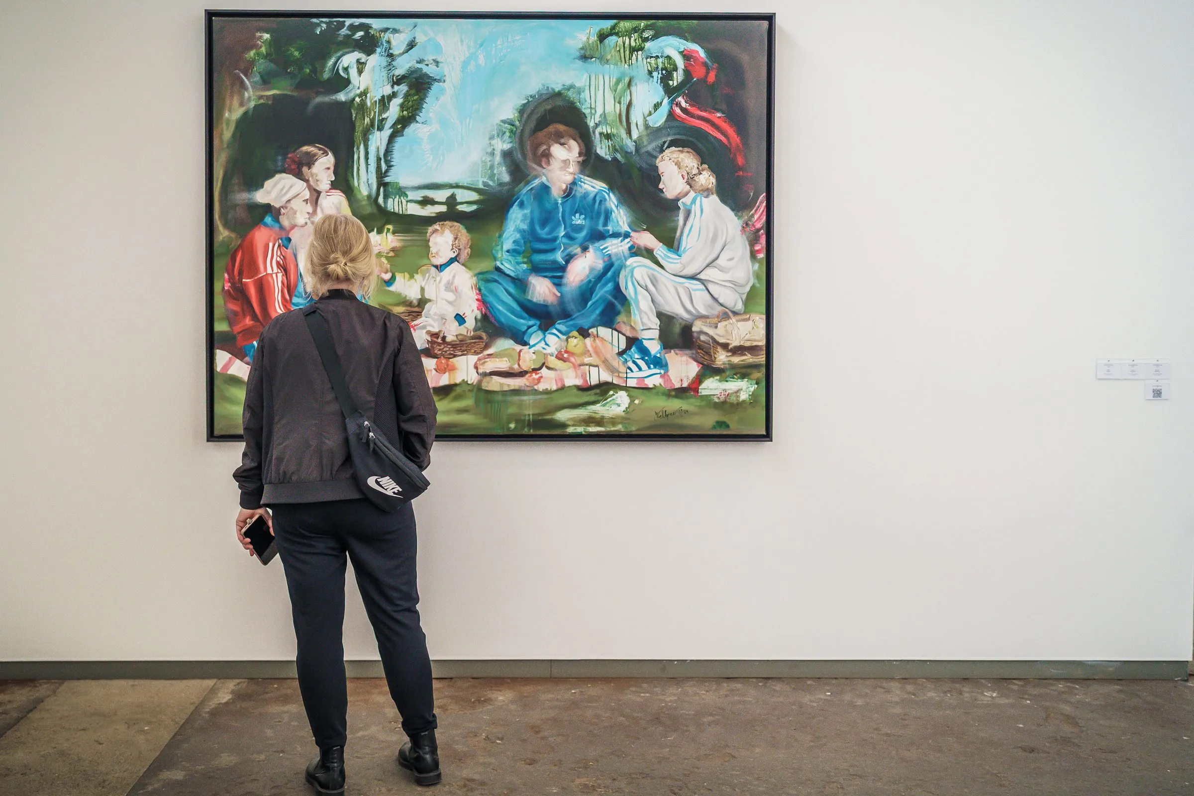 A visitor in front of a painting with a picnic scene in the greenery