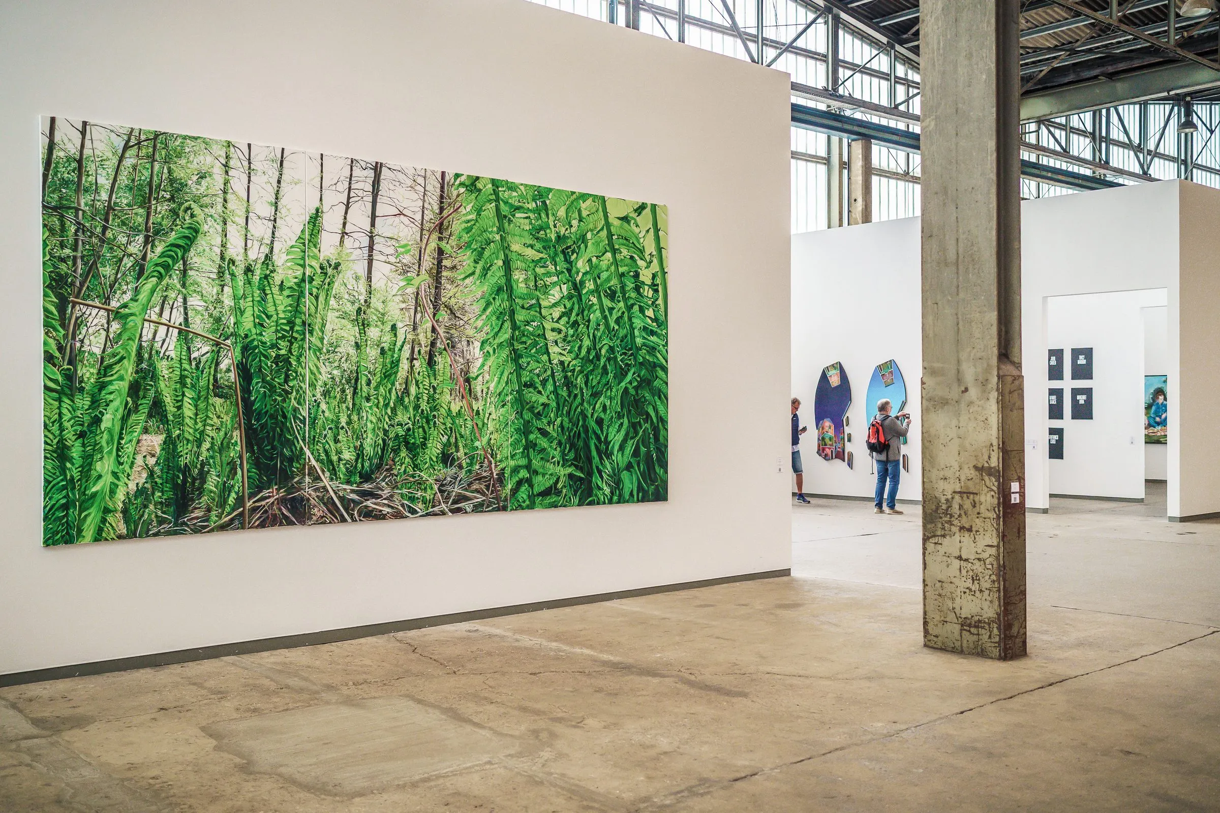 A large picture of dense green fern and forest floor on a white wall, a pillar on the right