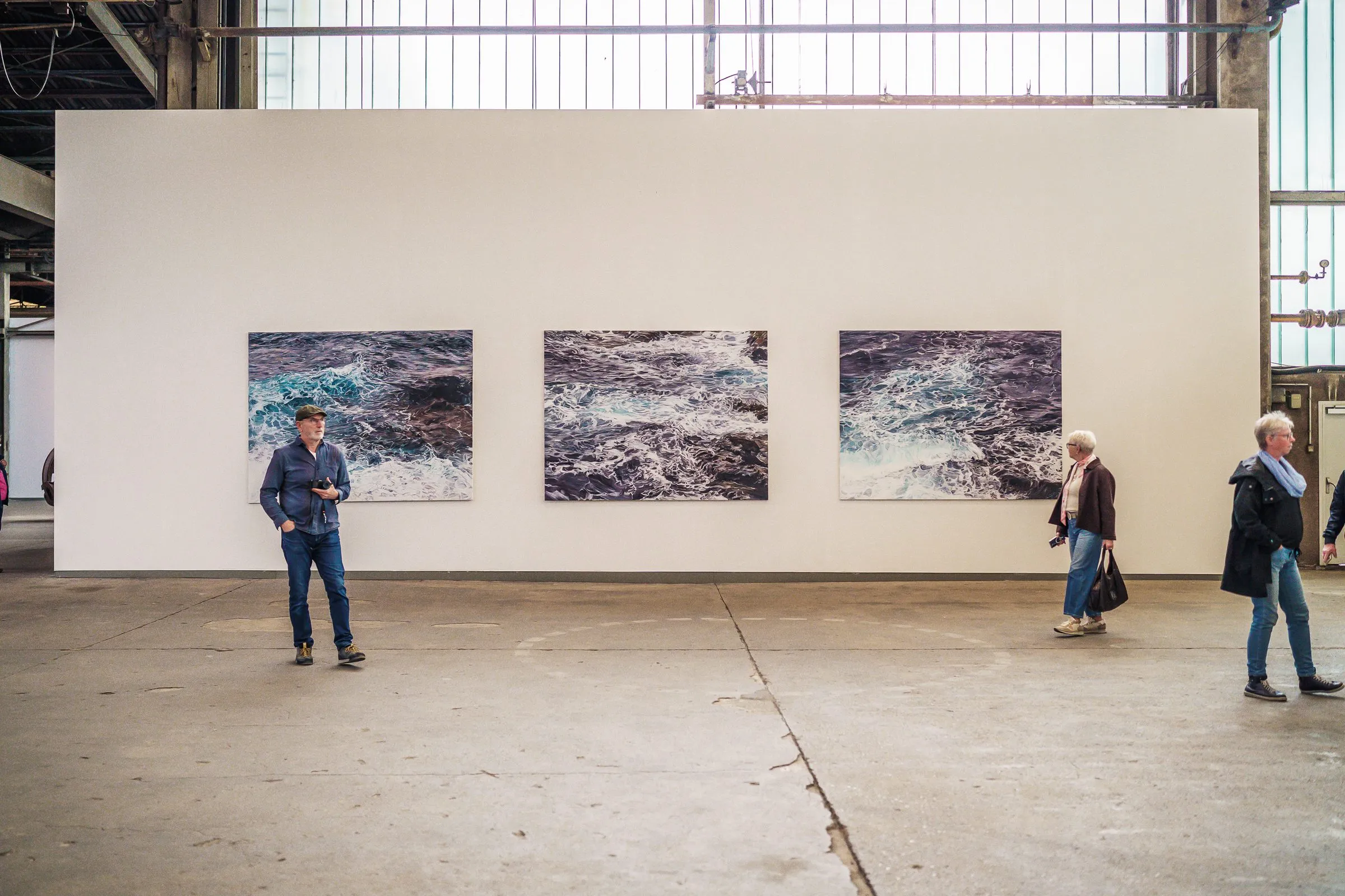 Three pictures of moving water side by side on a white wall, visitors in front