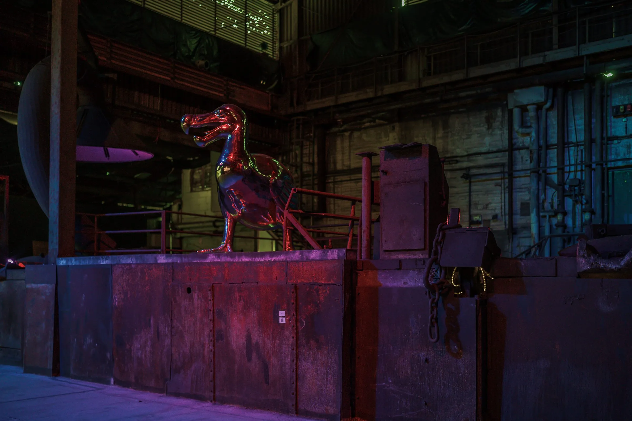 A dark hall in blue and red light, a sculpture like a dinosaur on a rusty wall