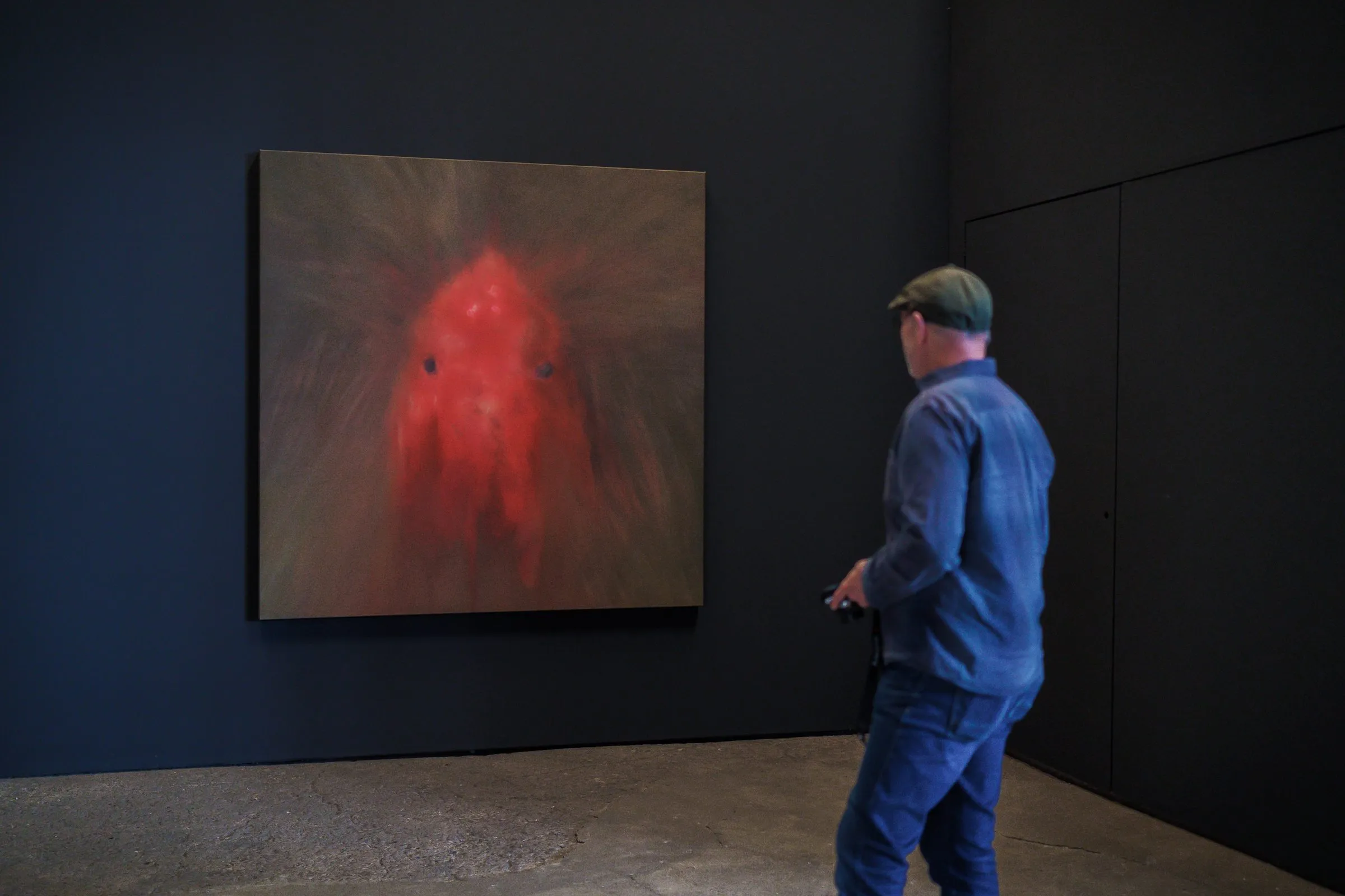 A man stands in a dark room in front of a picture with a blurred red shape