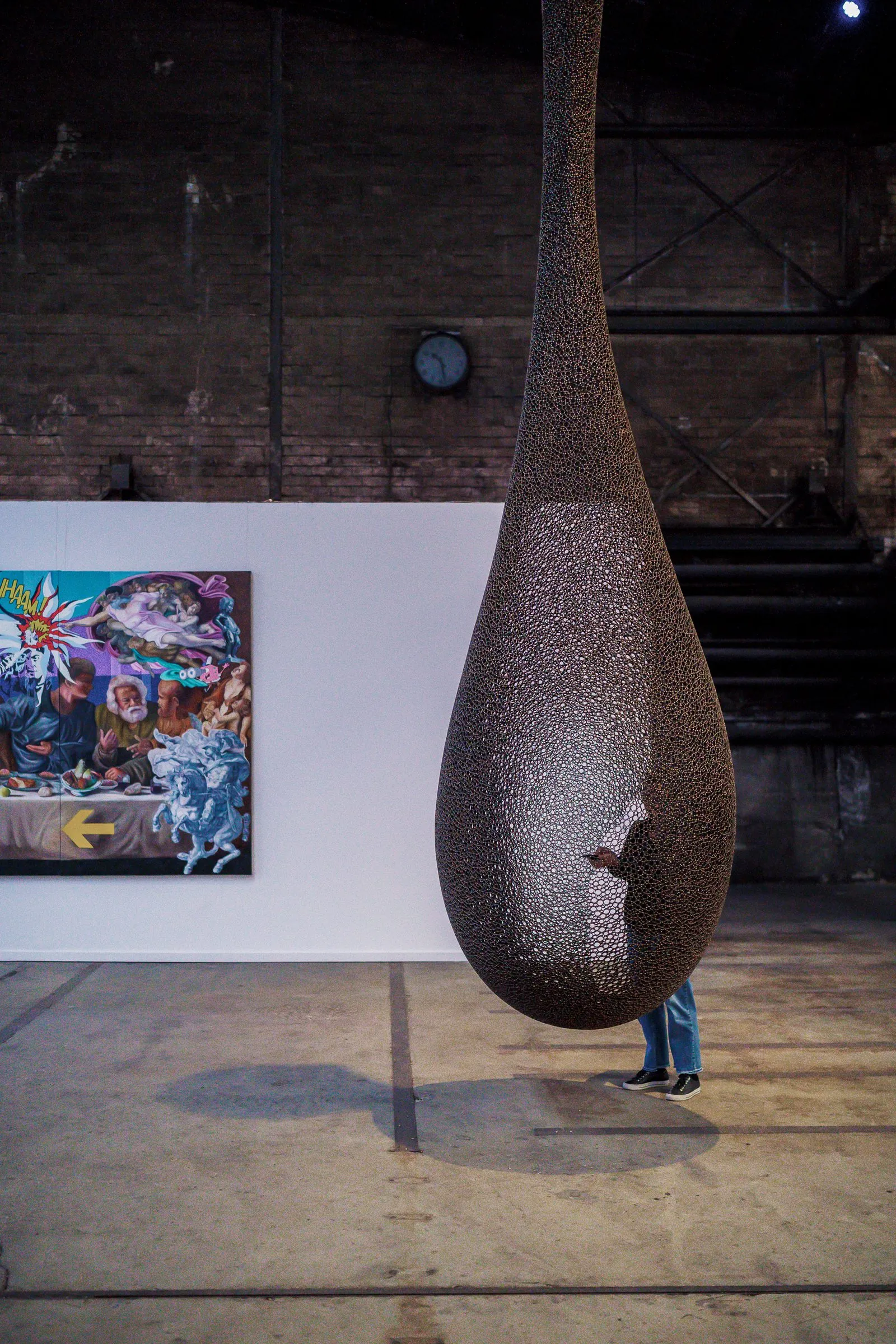 Portrait: a large teardrop-shaped shell of woven material hangs in the hall, a colourful picture behind
