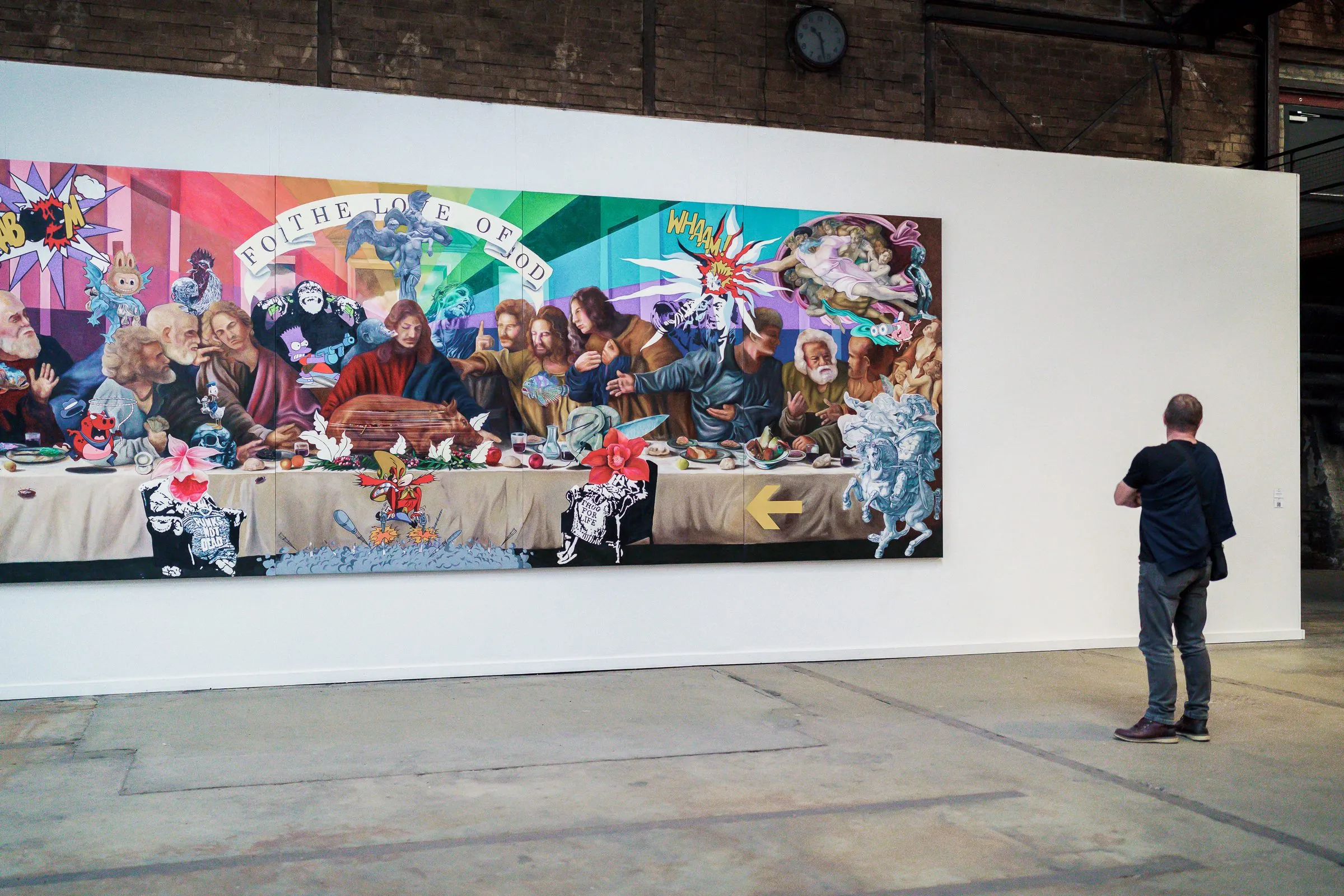 A very wide, colourful painting with a long table full of figures, a man stands in front