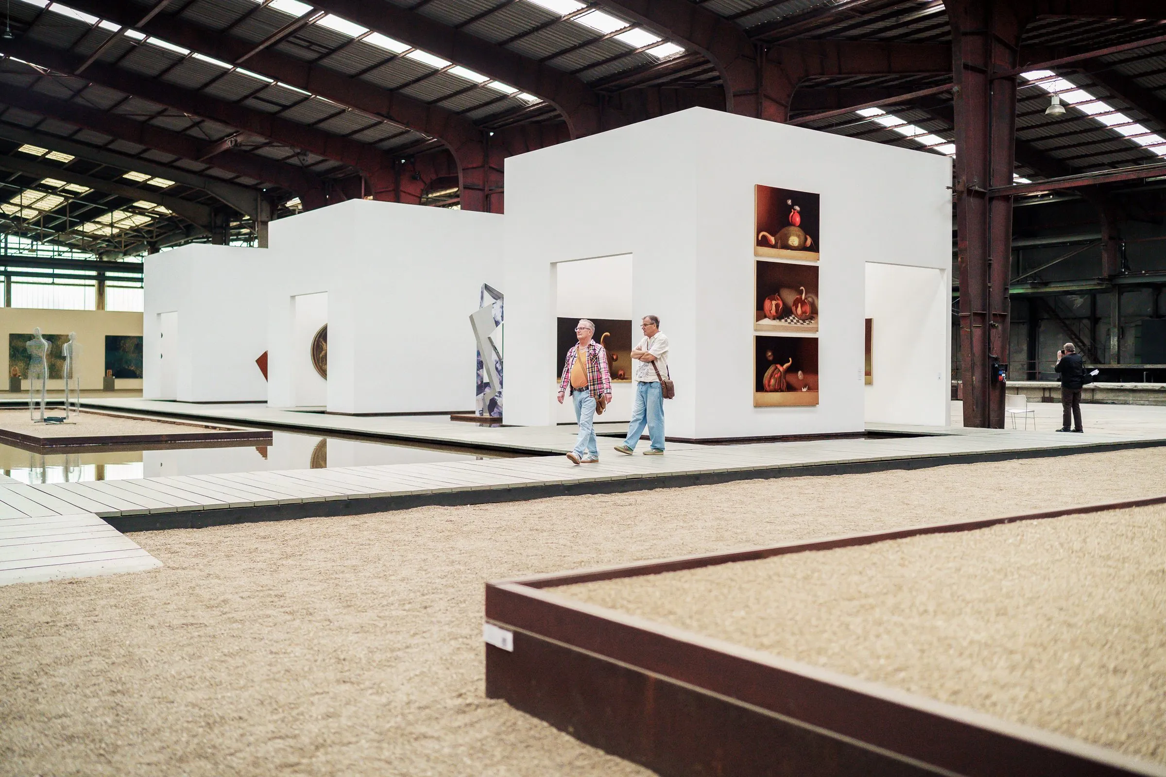 White room cubes in the hall, gravel areas with rusty edges, visitors on the way