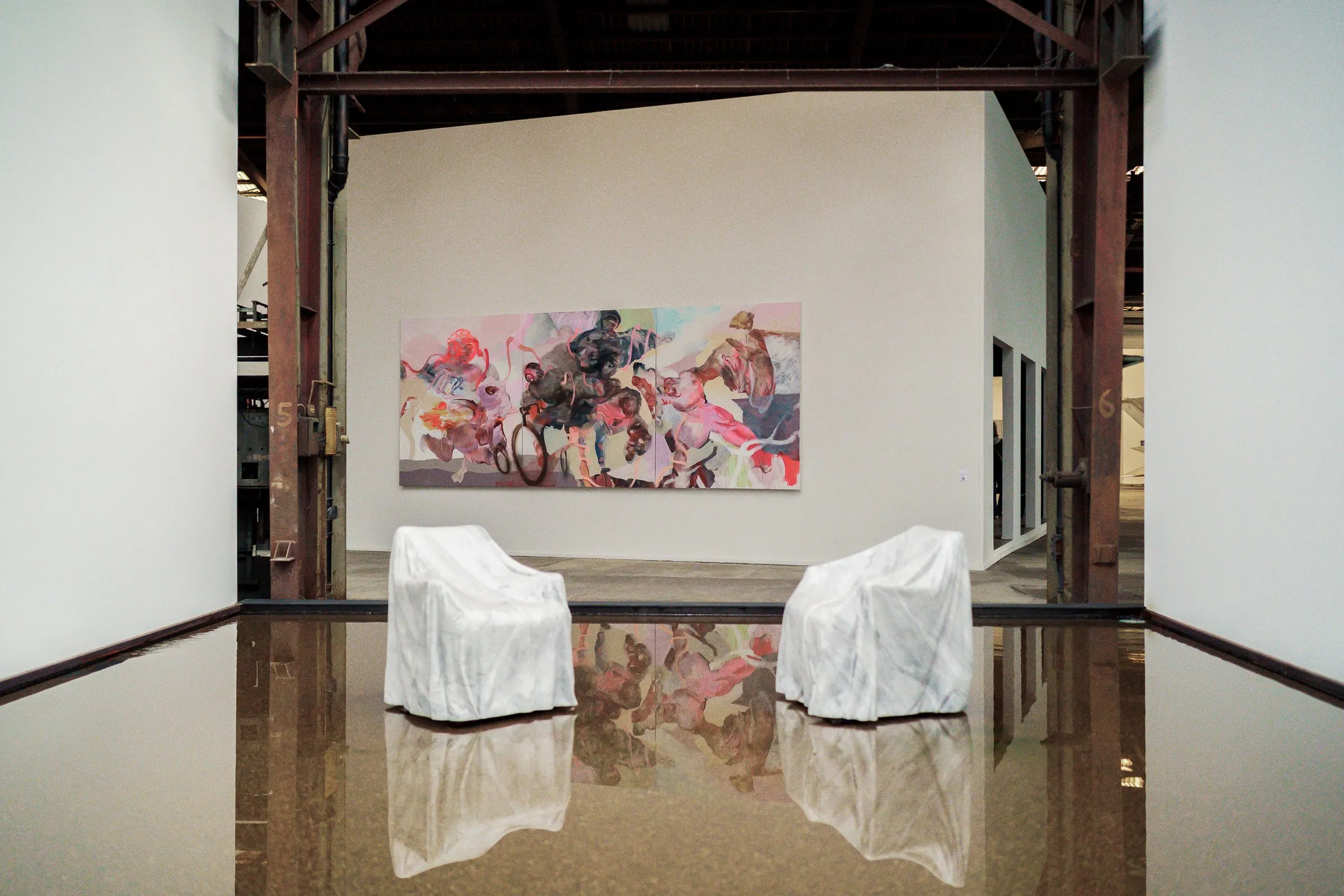 Two white-draped armchairs in the water in front of a large, colourful painting