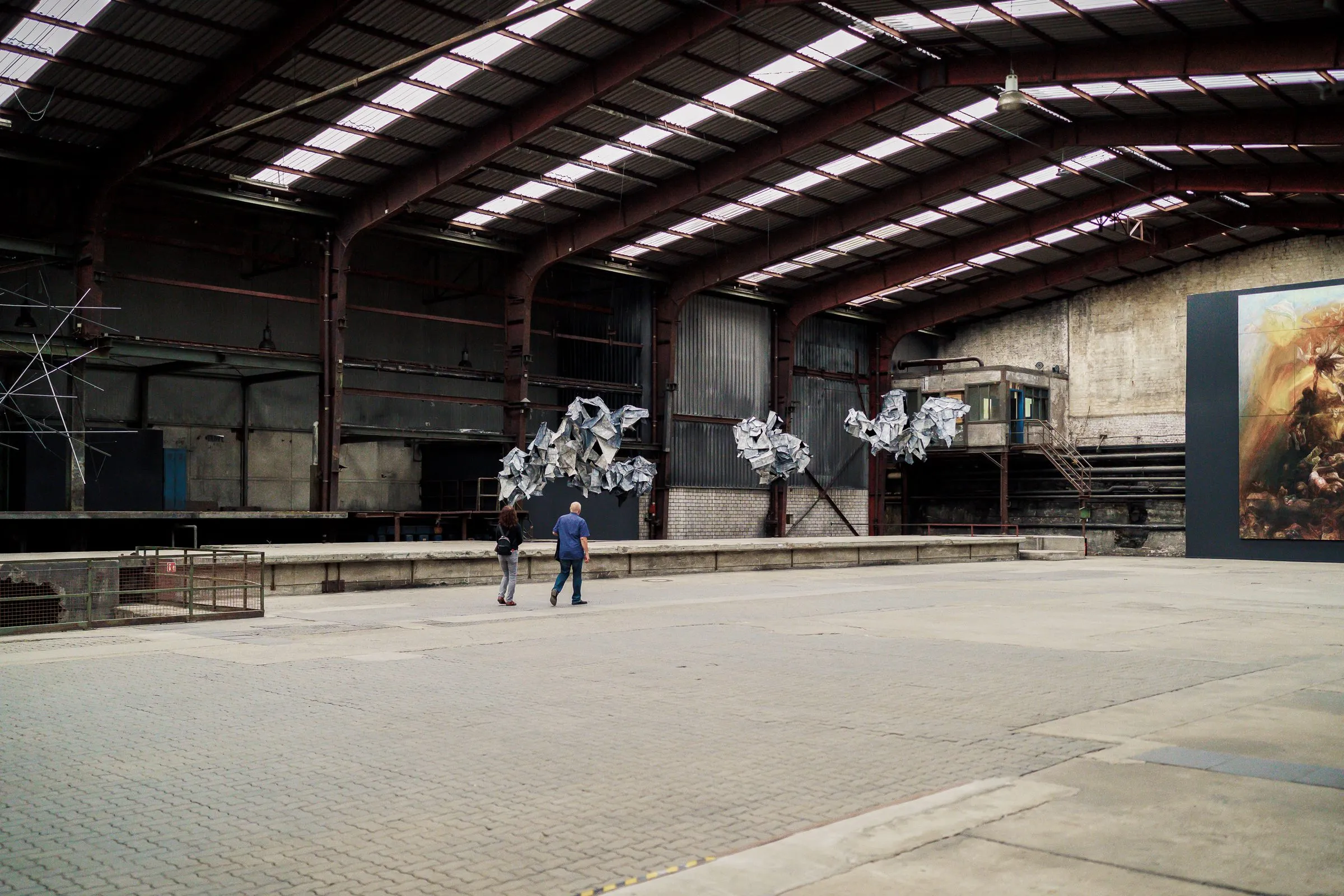 An empty, wide hall, silver crumpled forms under the roof, a large picture on the right