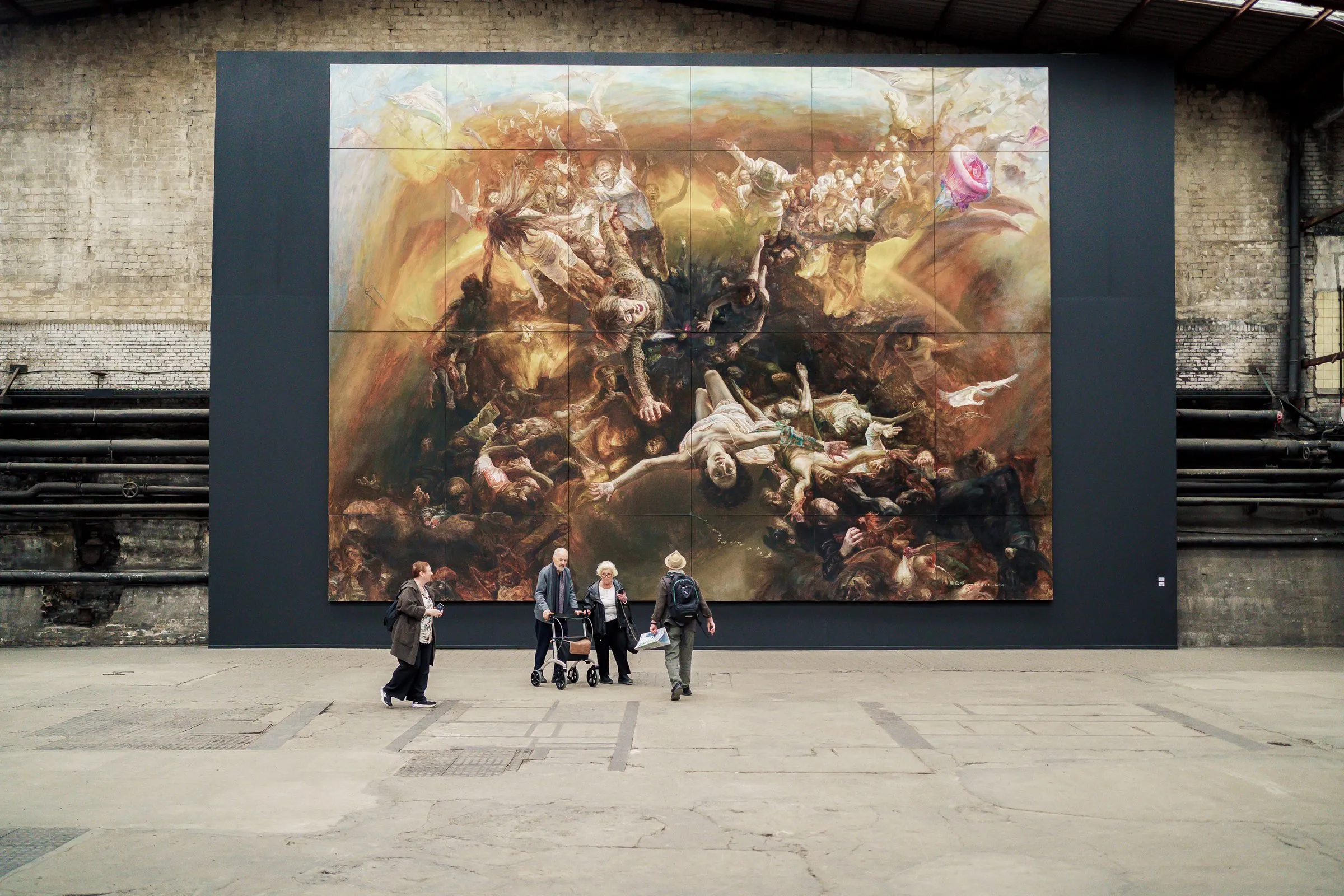 The huge painting Eye in the Sky on a dark wall, a small group of visitors in front