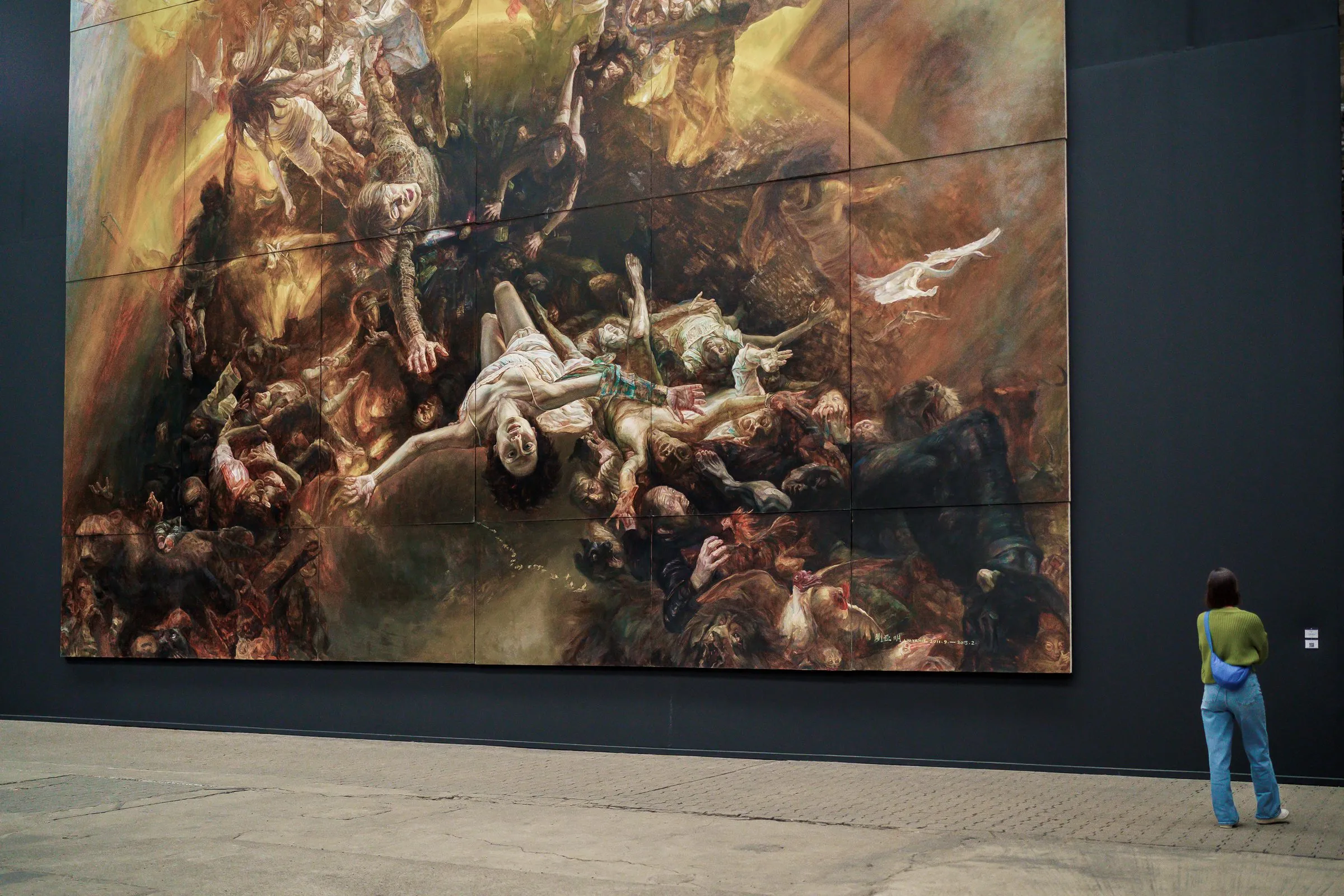 A visitor stands at the lower right edge of a huge painting of tumbling bodies and barely reaches its lower edge