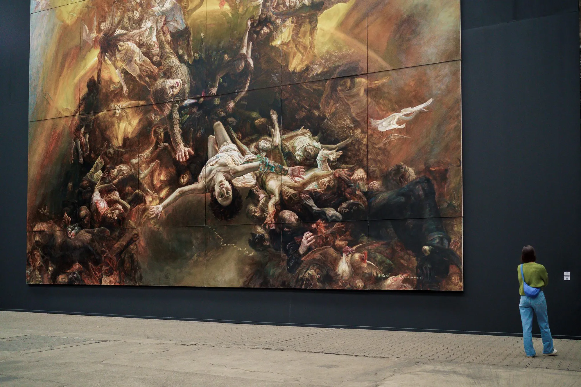 A visitor stands at the lower right edge of a huge painting of tumbling bodies and barely reaches its lower edge