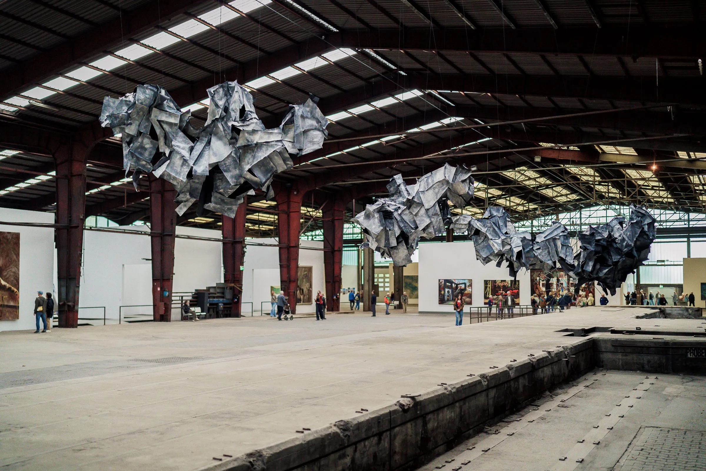 Shiny silver crumpled forms float like clouds under the hall roof above a pit