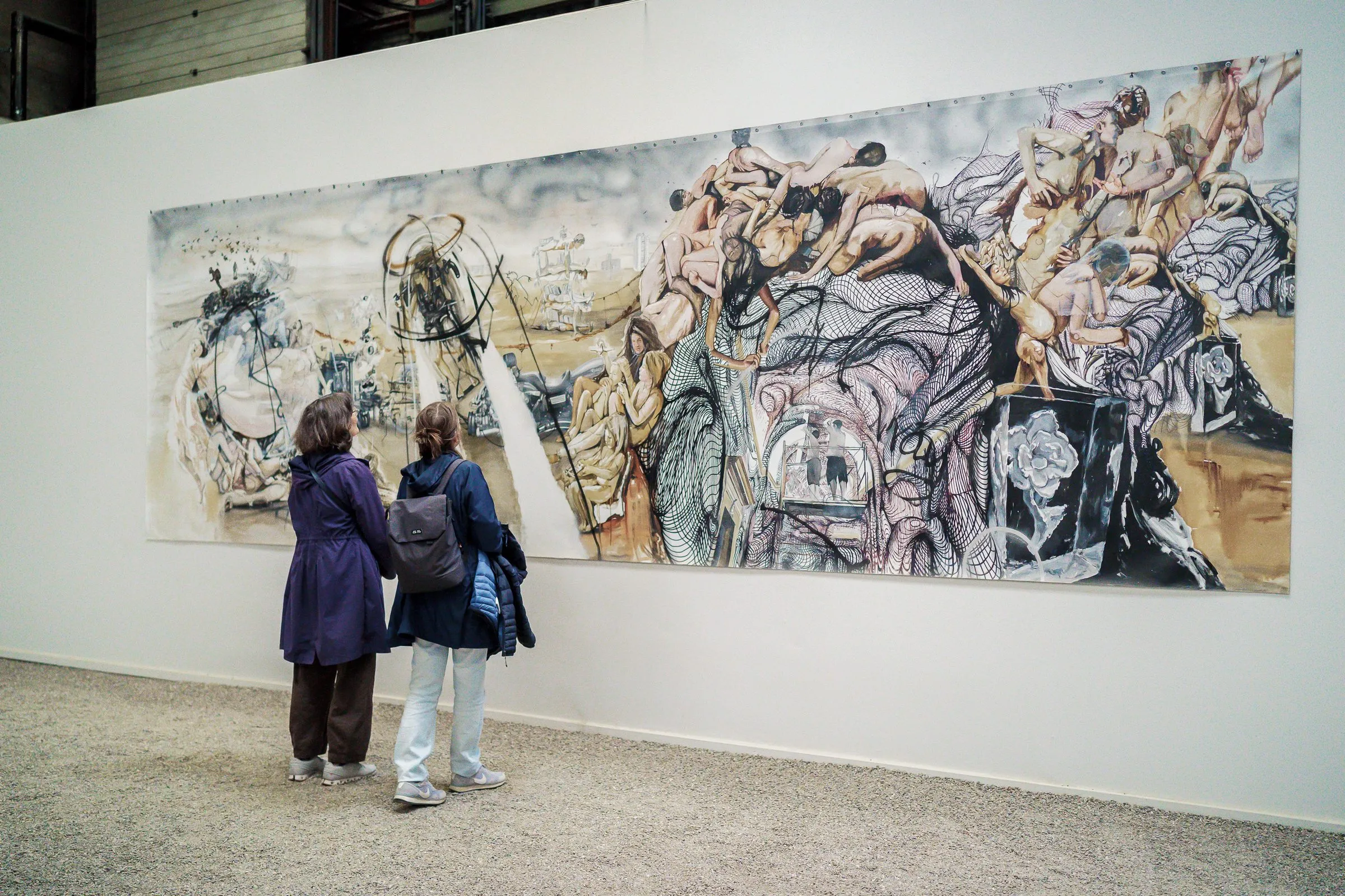 Two women look at a long drawing with intertwined bodies