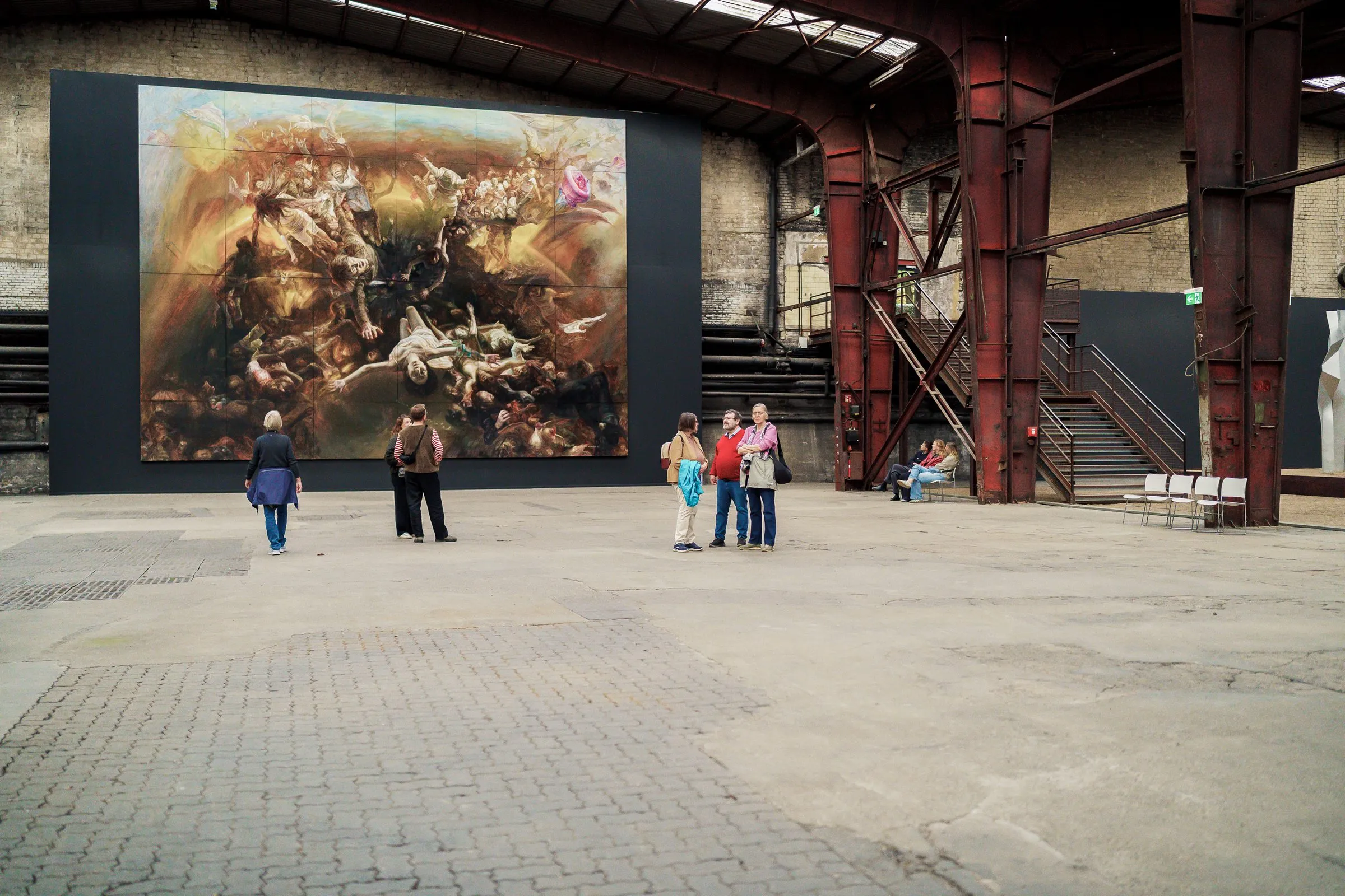 The painting in the hall between red steel columns, small groups of visitors spread in front