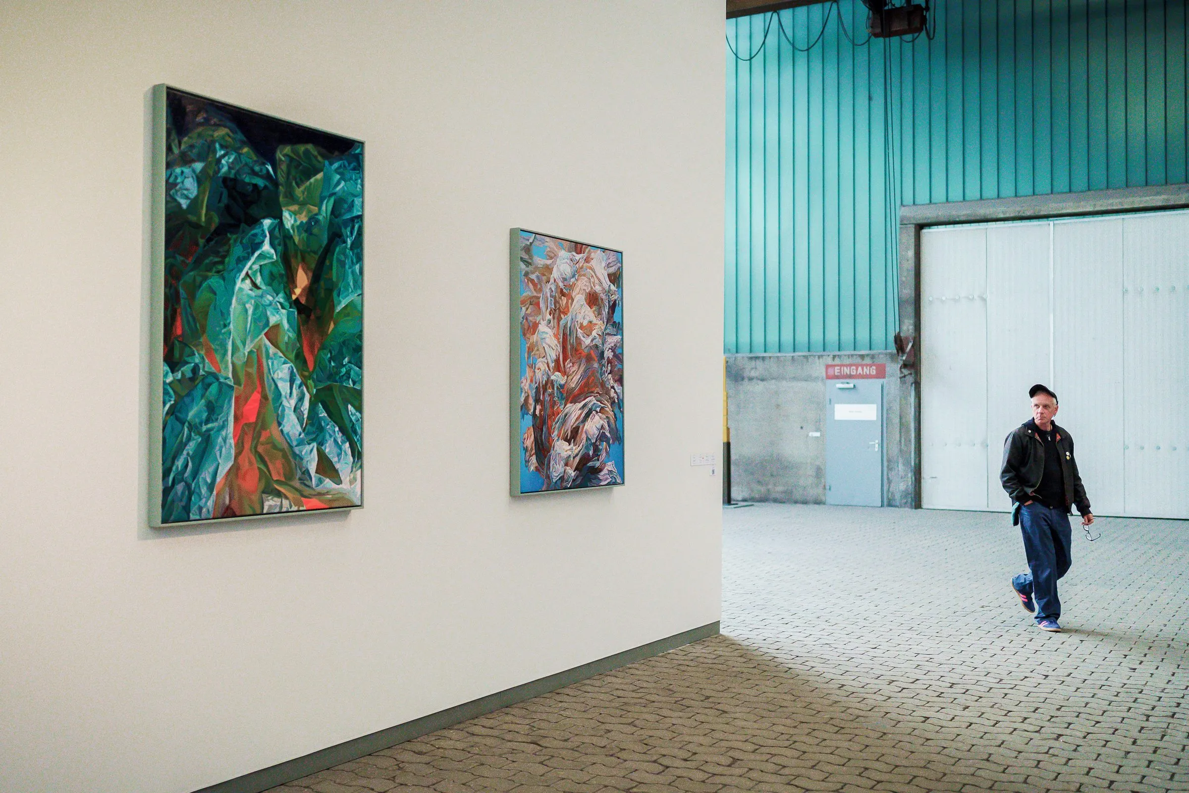 Two colour-intense paintings on a white wall, a man walks past towards the hall door