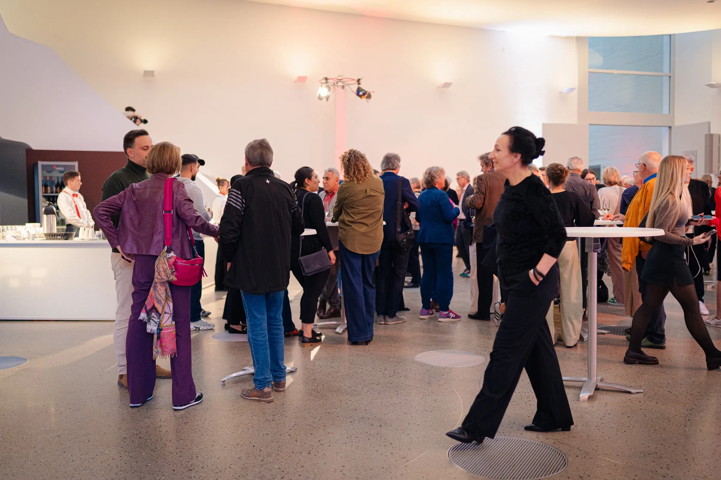 Guests in the bright entrance hall with a curved staircase, standing tables, conversations