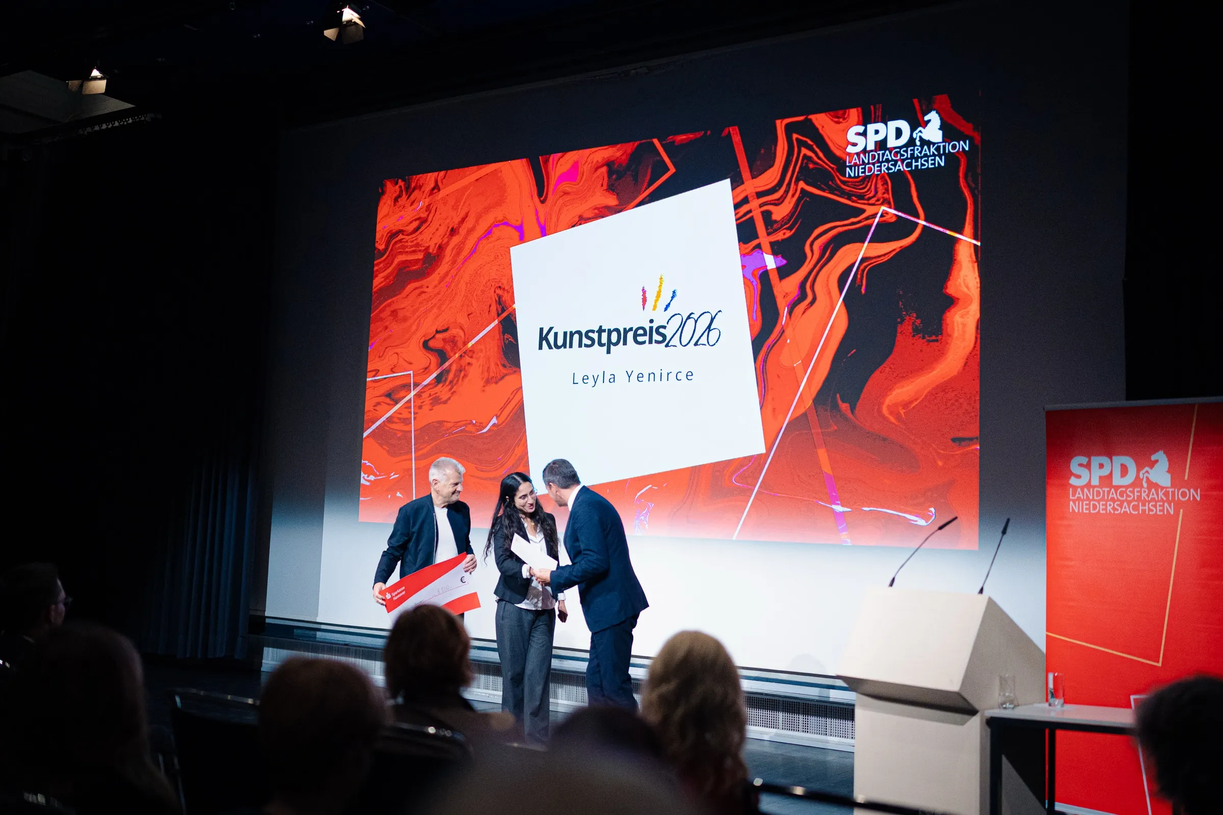 Stefan Politze, Leyla Yenirce and Olaf Lies on stage as the certificate is handed over