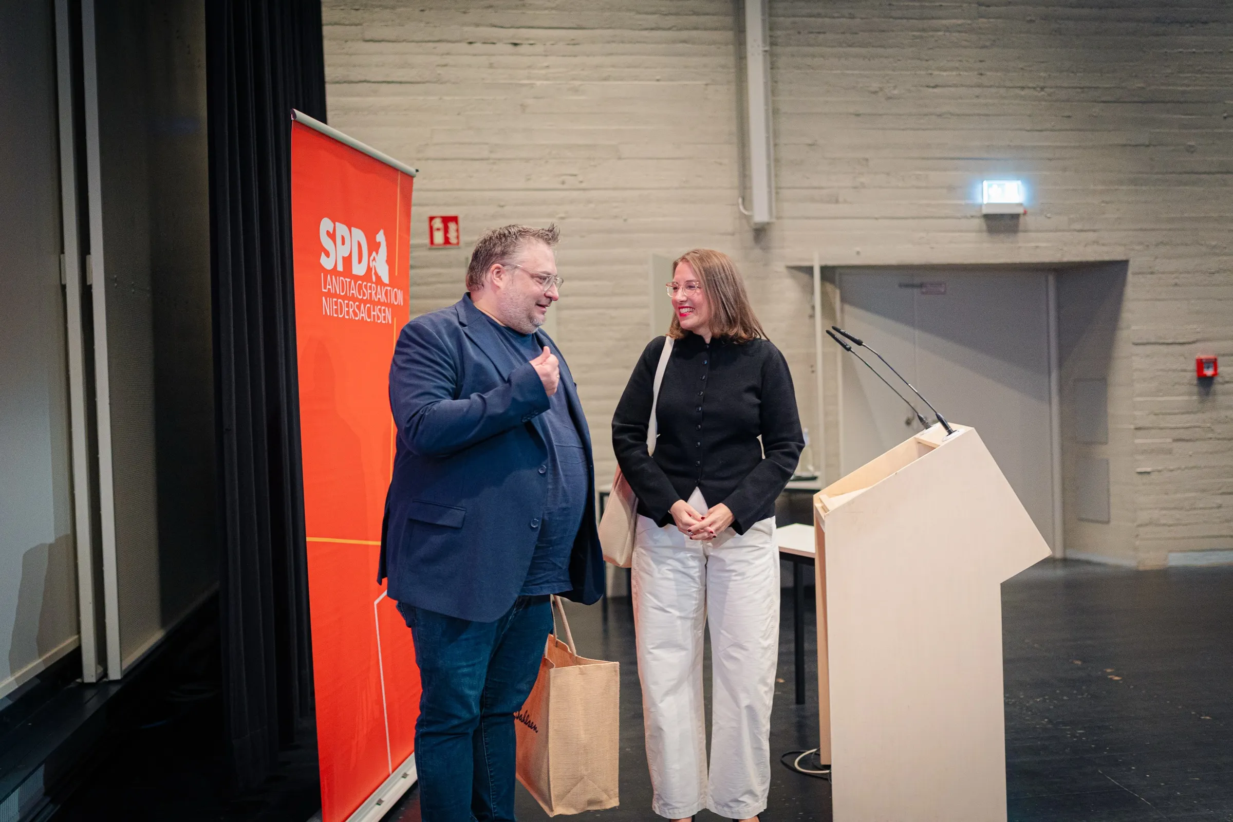Two guests talking next to the lectern and the red banner of the SPD parliamentary group