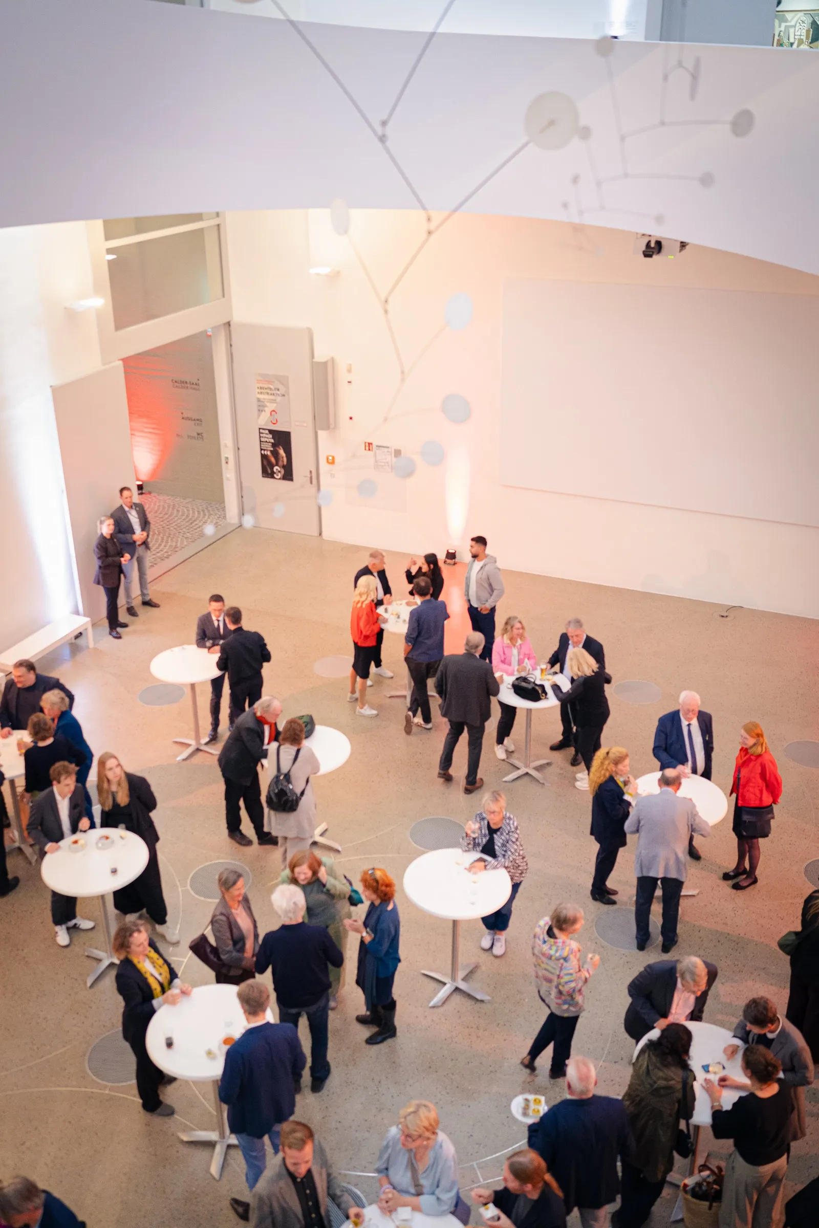 Portrait format: looking down on the foyer with round standing tables and many guests