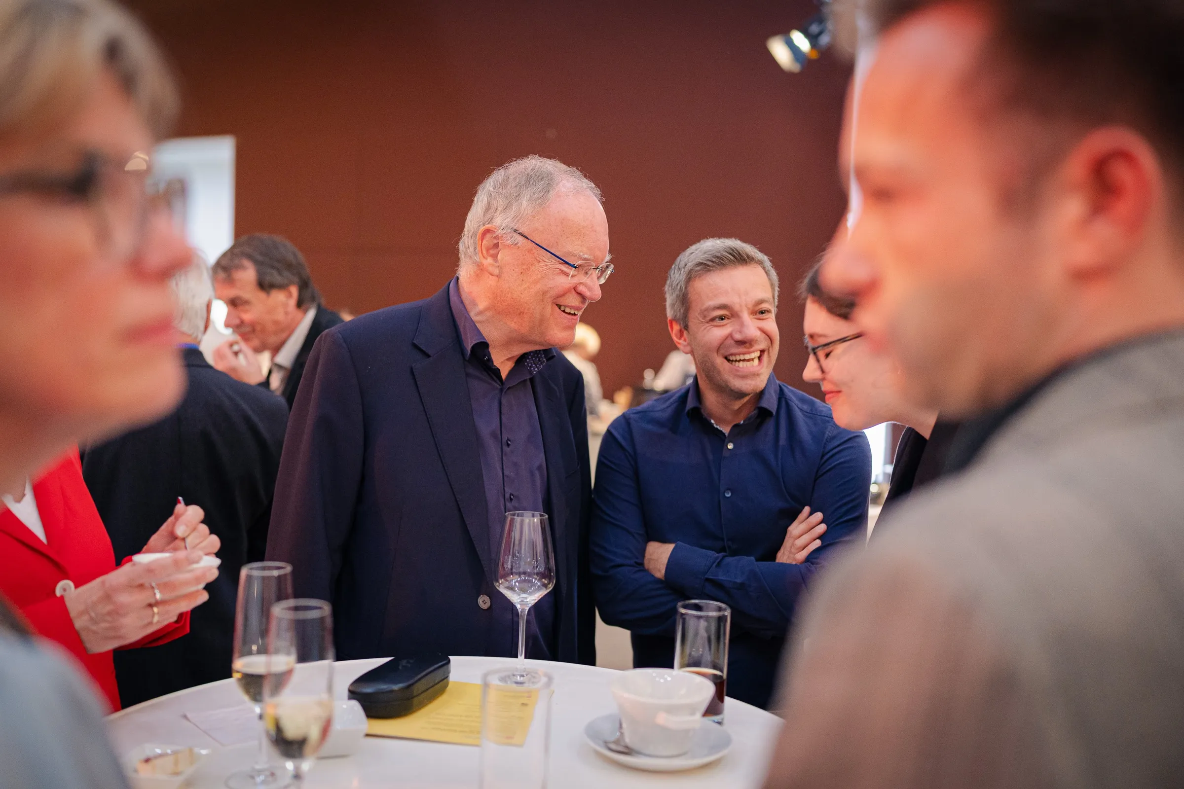 Stephan Weil laughing at a standing table, next to him a man in a blue shirt, other guests blurred in the foreground