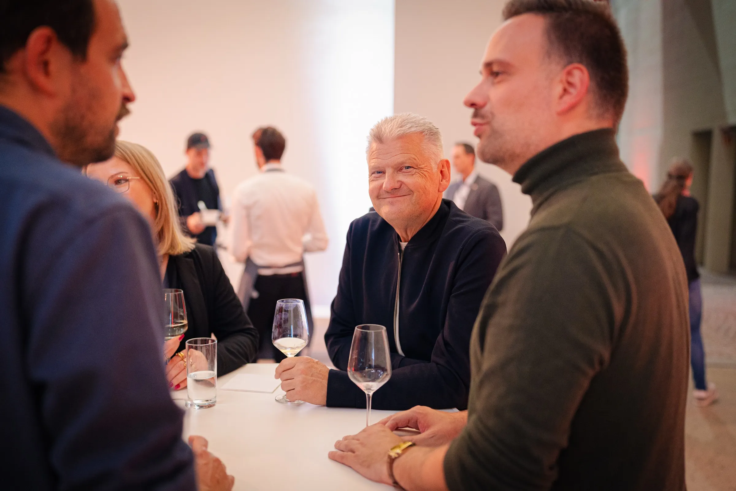 Stefan Politze smiling at a standing table with wine glasses, conversation partners on either side