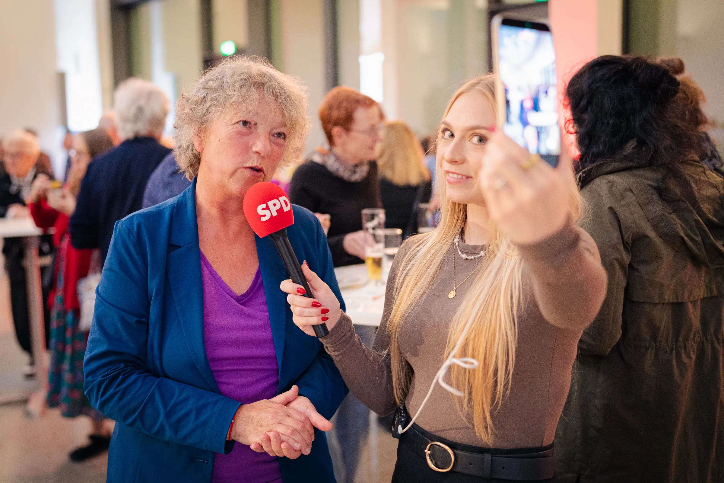 Hanna Naber speaking into a red SPD microphone, a young woman filming the interview on a smartphone