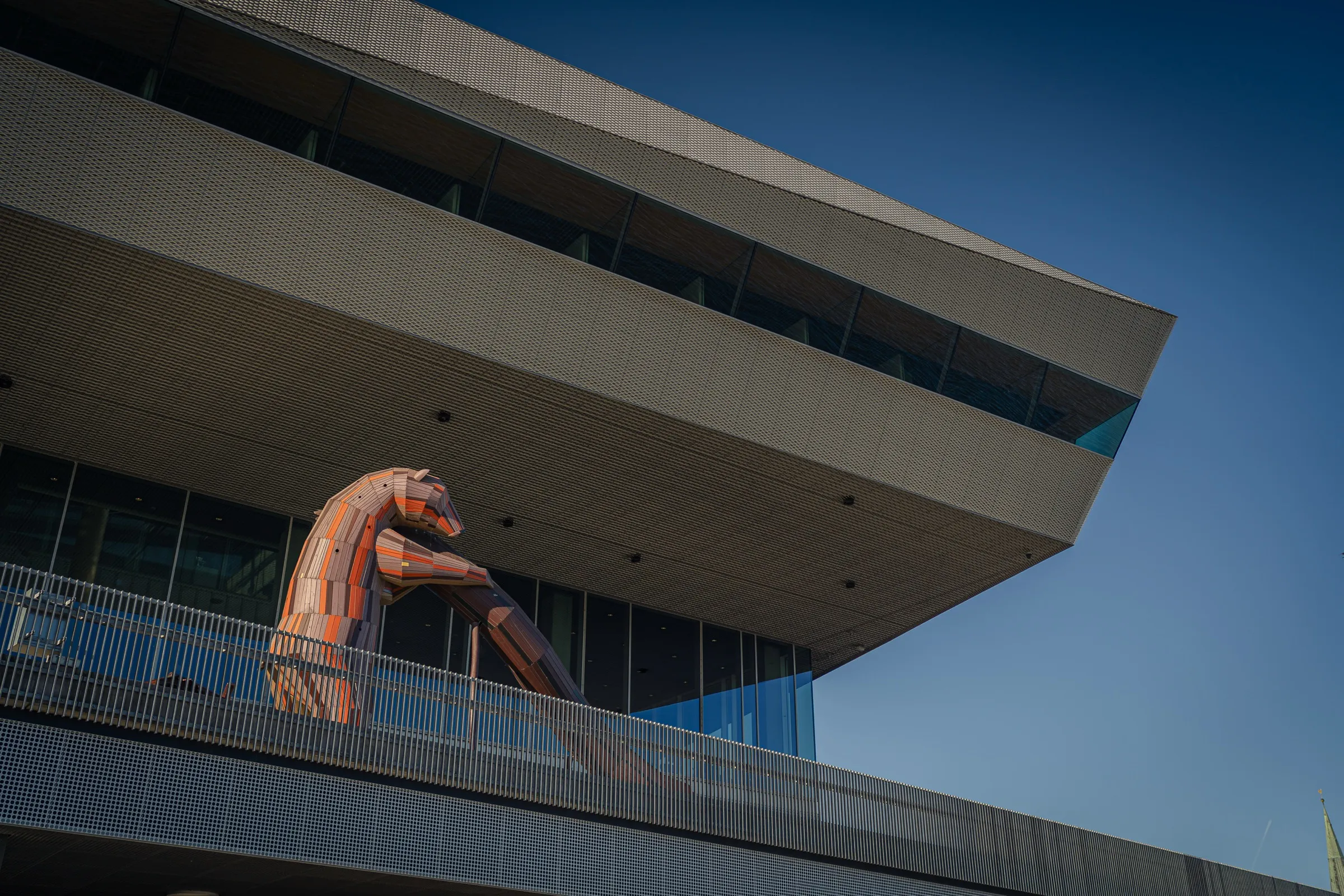 The far-cantilevered underside of Dokk1 above a parapet, a large animal figure on it, blue sky