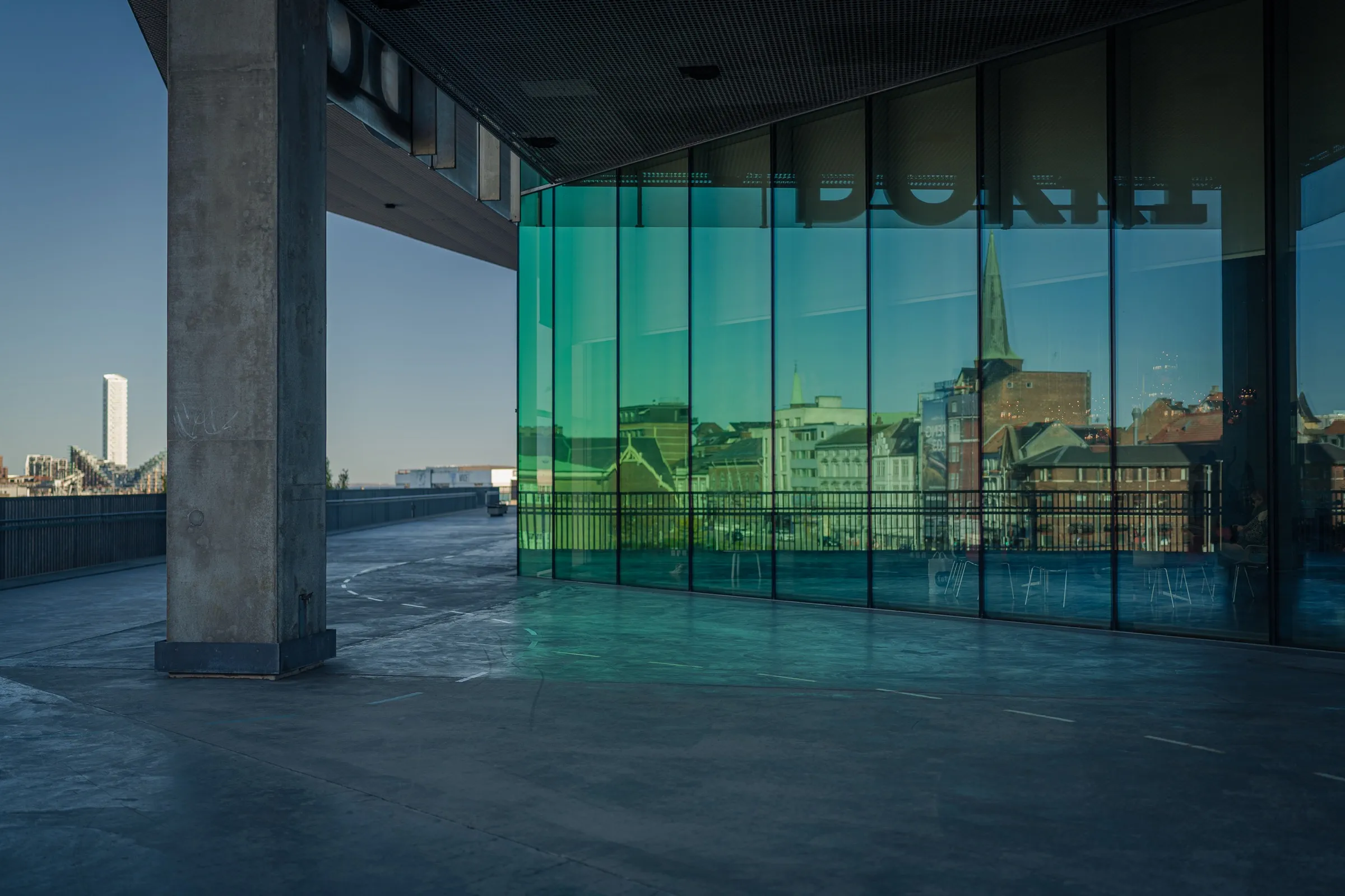 A concrete column in front of the green, reflective glass facade showing the city