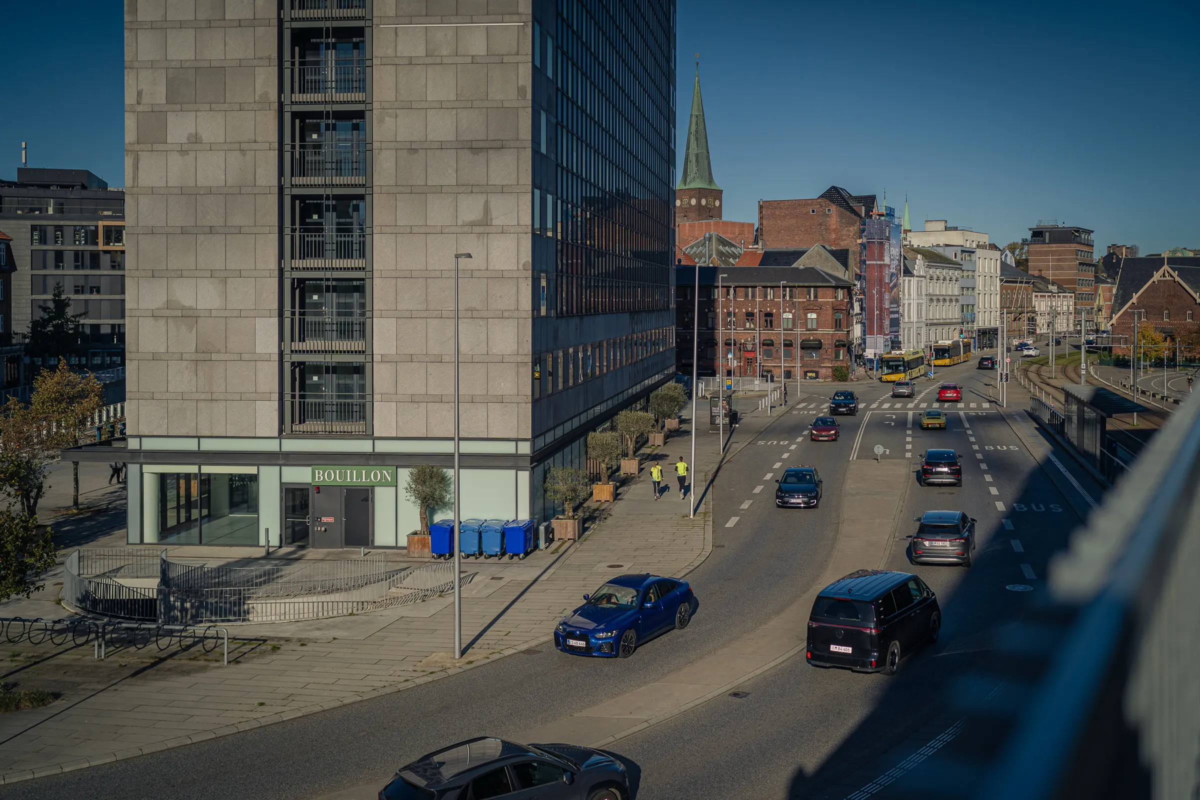 Looking down on a road with cars, an office building on the left, the old town with a church spire behind