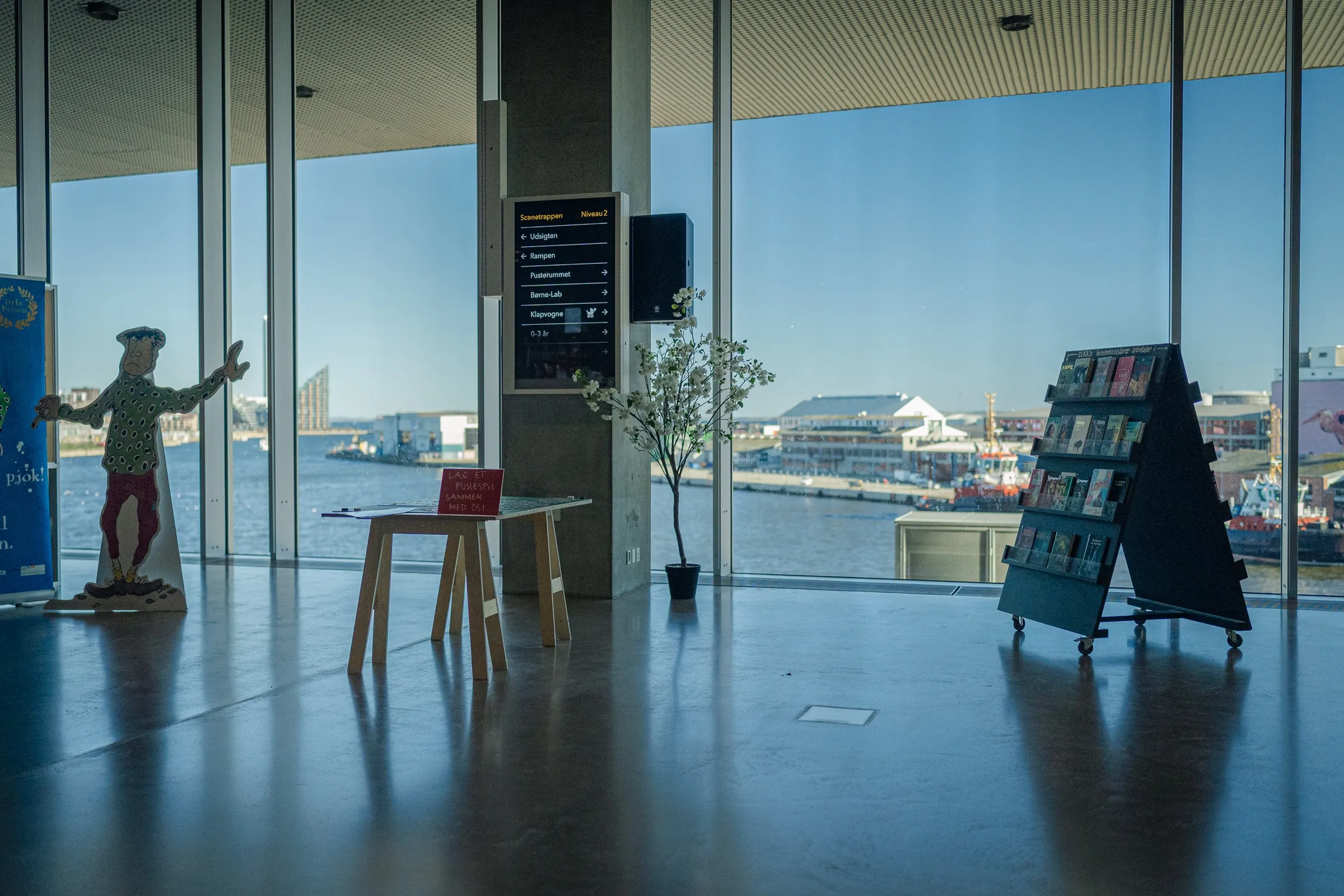 Floor-to-ceiling windows overlooking the harbour, furniture and a magazine rack in front