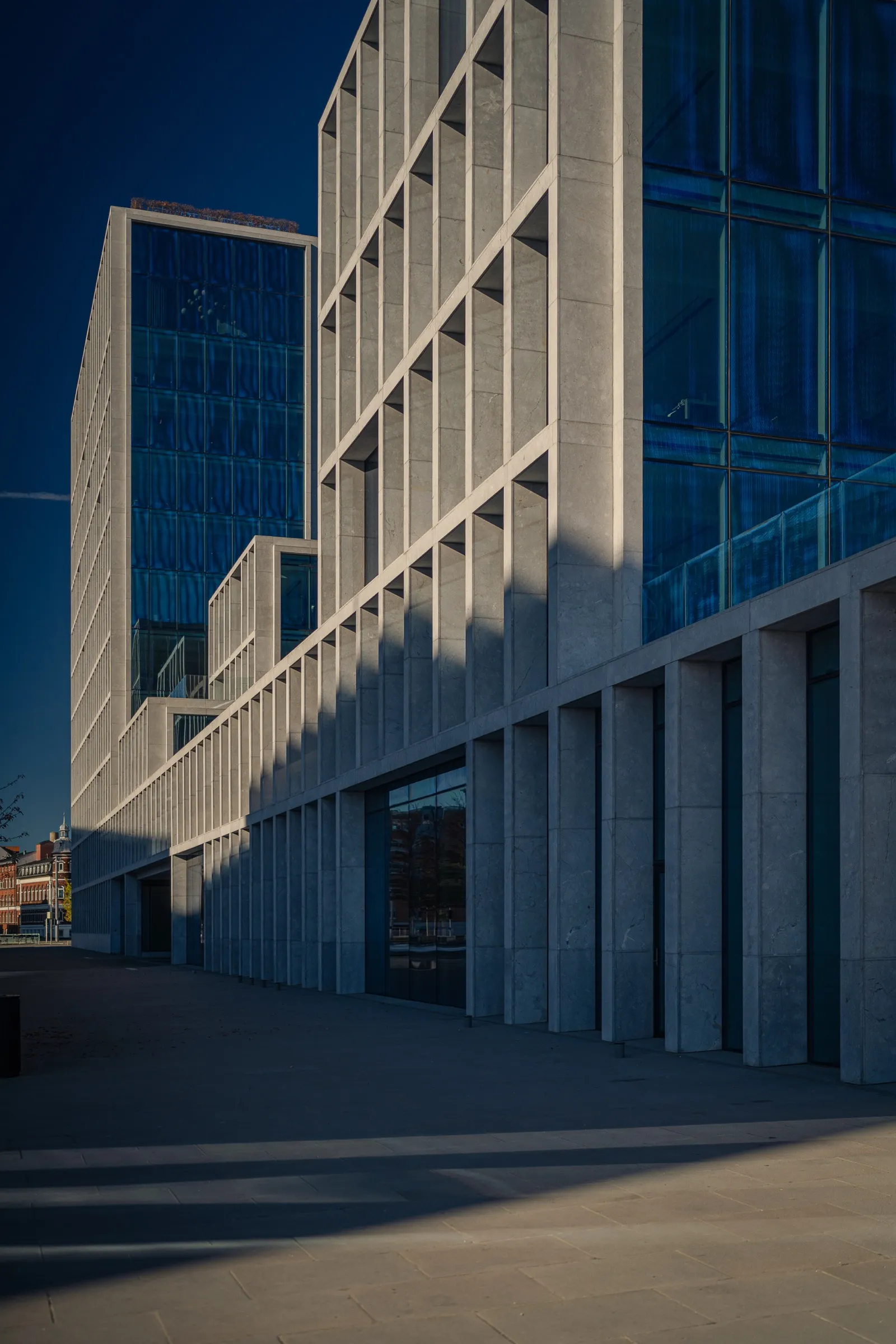Portrait: a natural stone facade with deep recesses, blue glass in shadow behind
