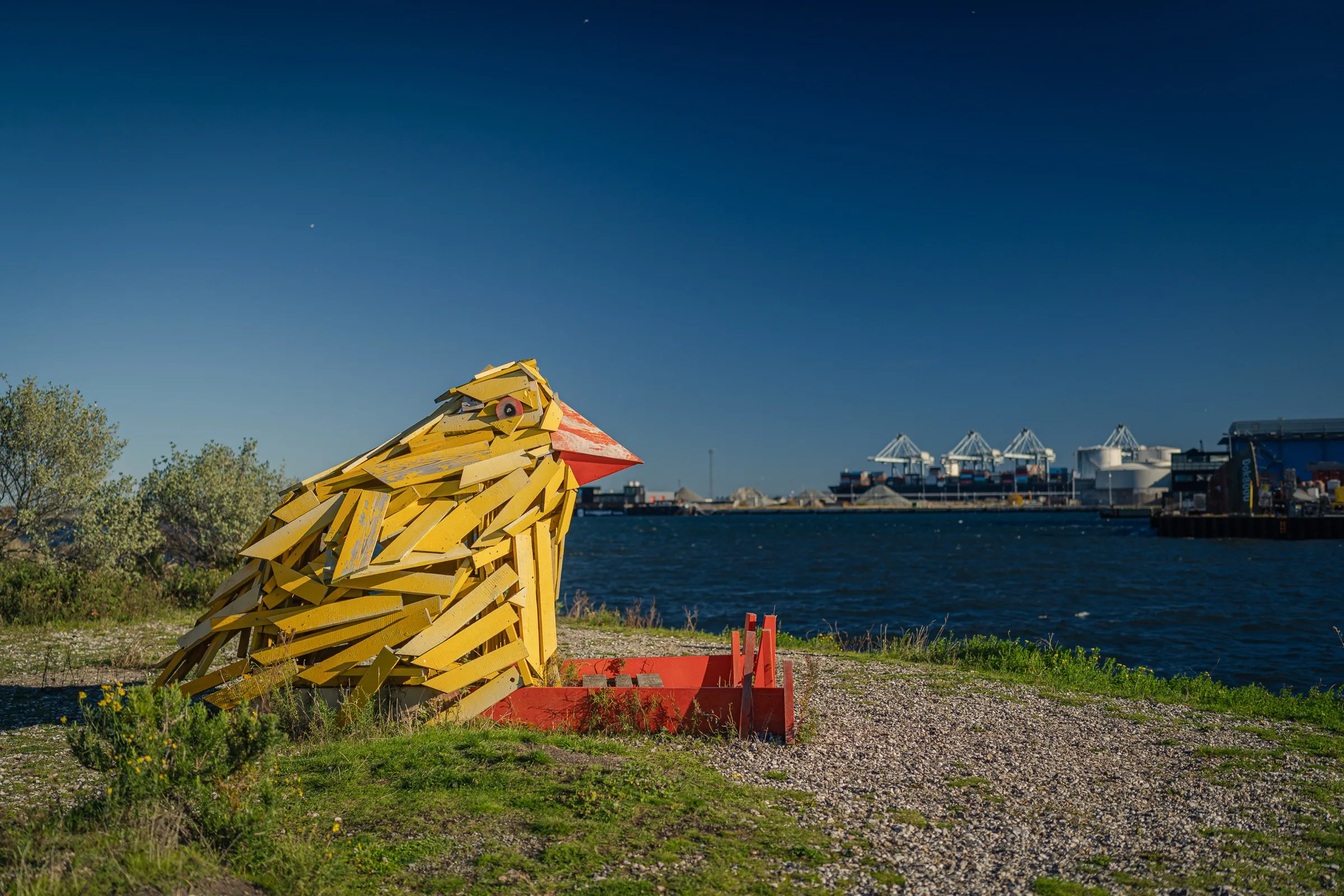 A large yellow bird figure made of wood on a meadow by the water
